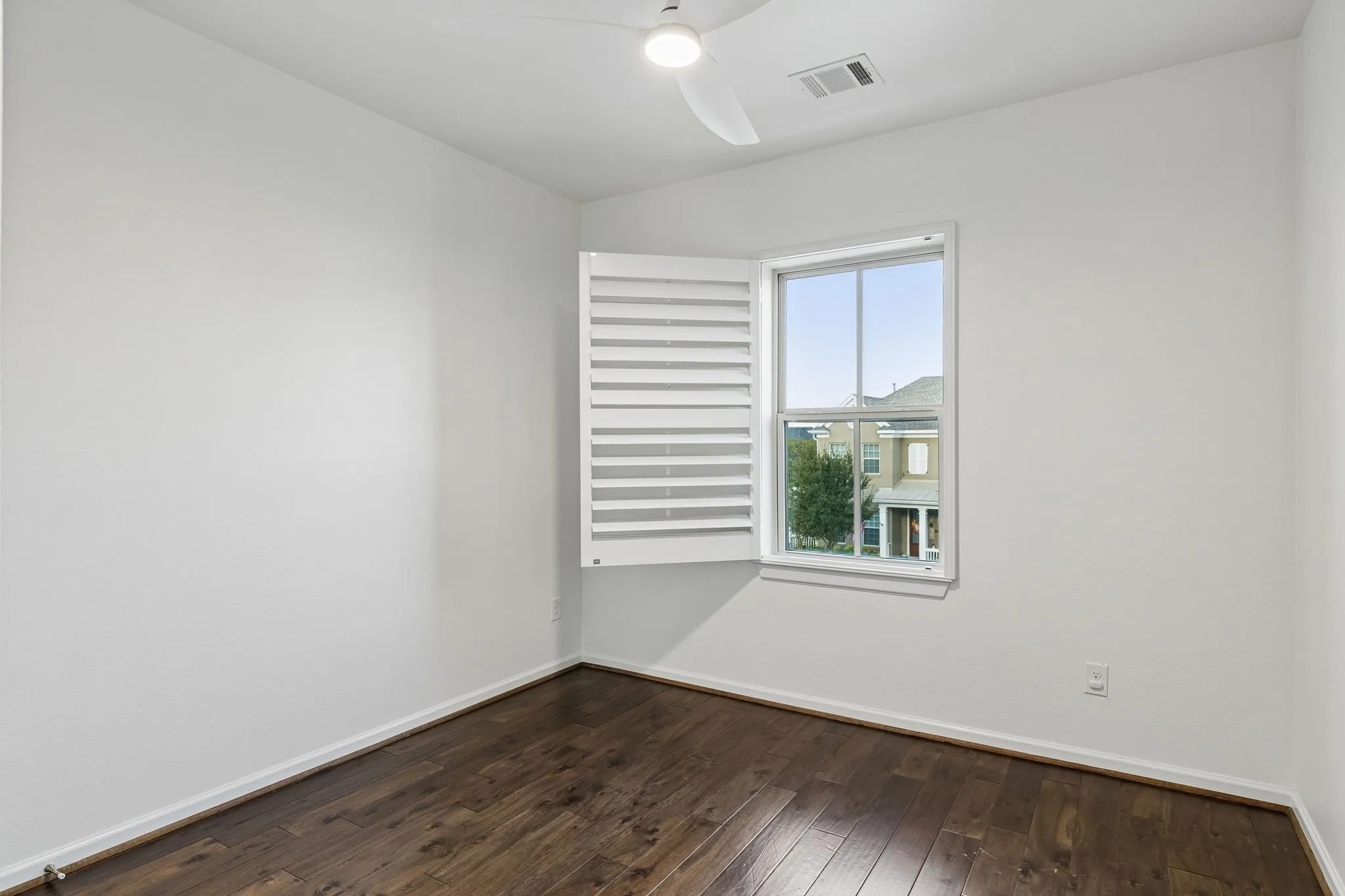 Wood-finish flooring, white walls, and a window with white plantation shutters