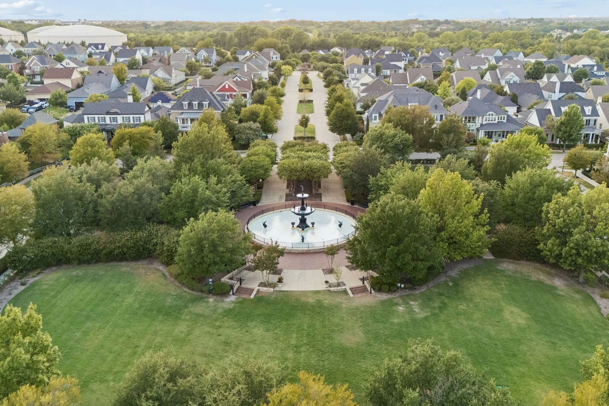 Expansive green space featuring a central fountain, paved walkways, and mature trees