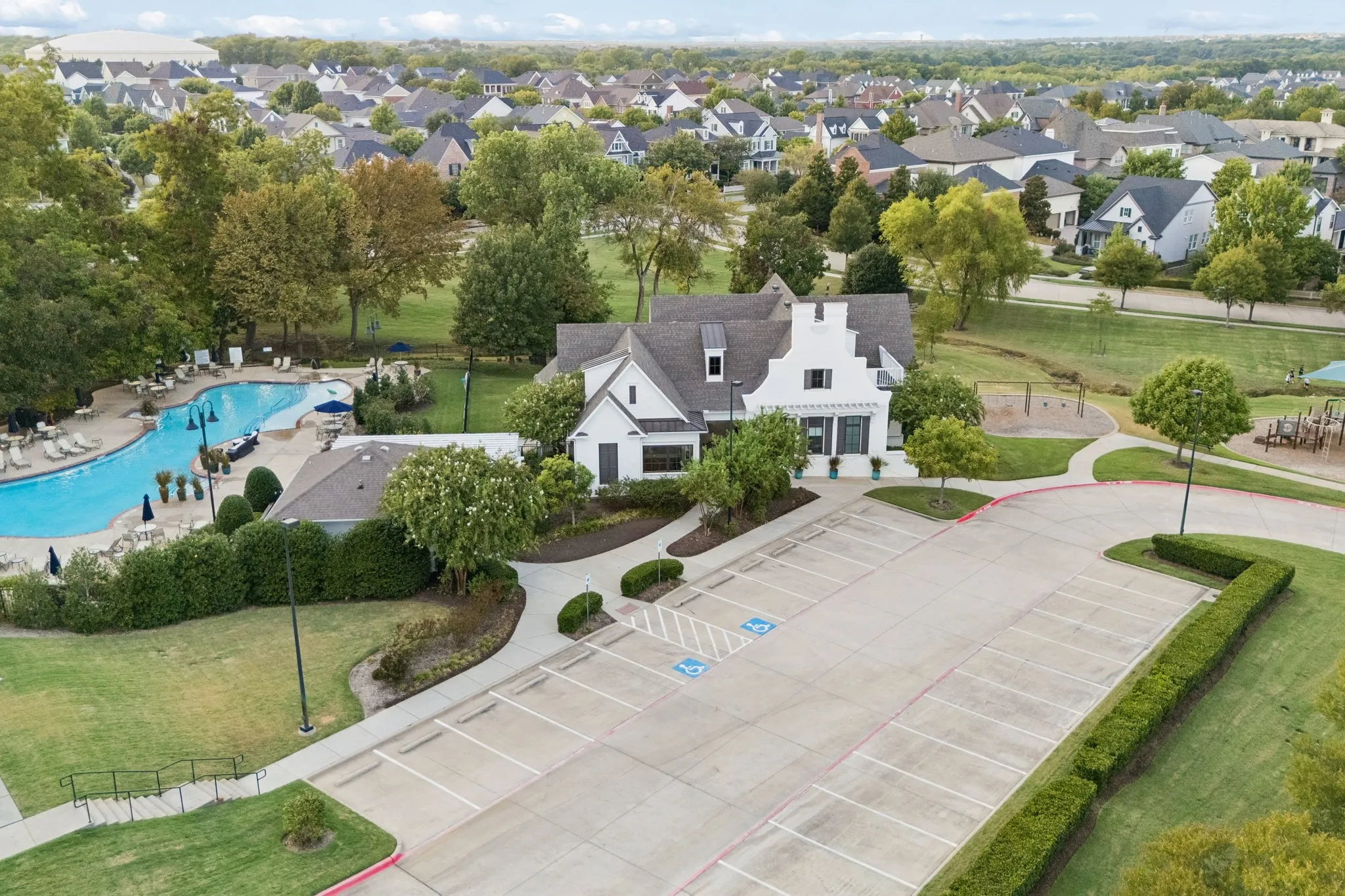 Community building featuring gabled roofs, a swimming pool, and dedicated parking
