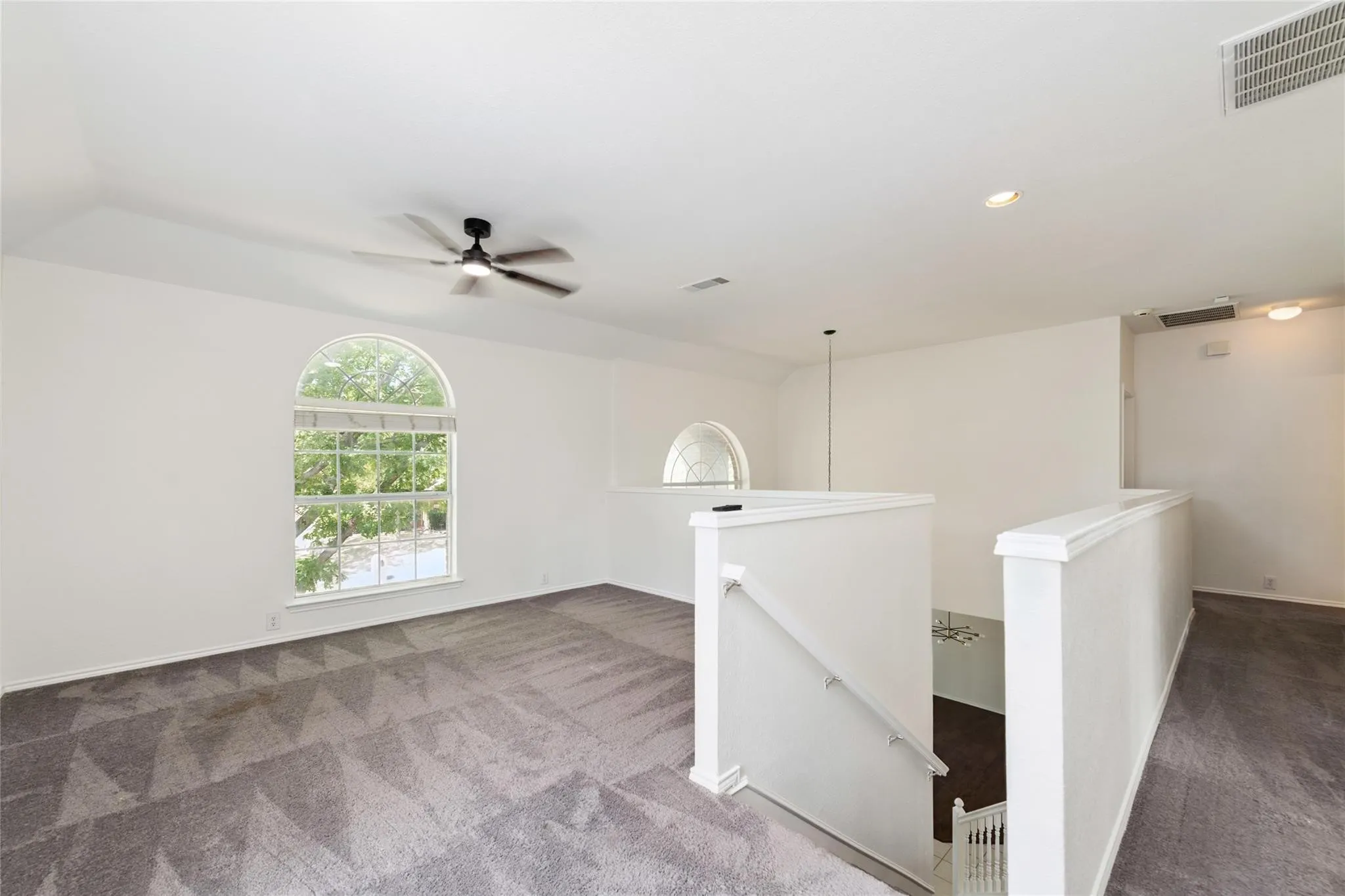 Carpeted loft area featuring an arched window, ceiling fan, recessed lighting, and a white balustrade overlooking a lower level
