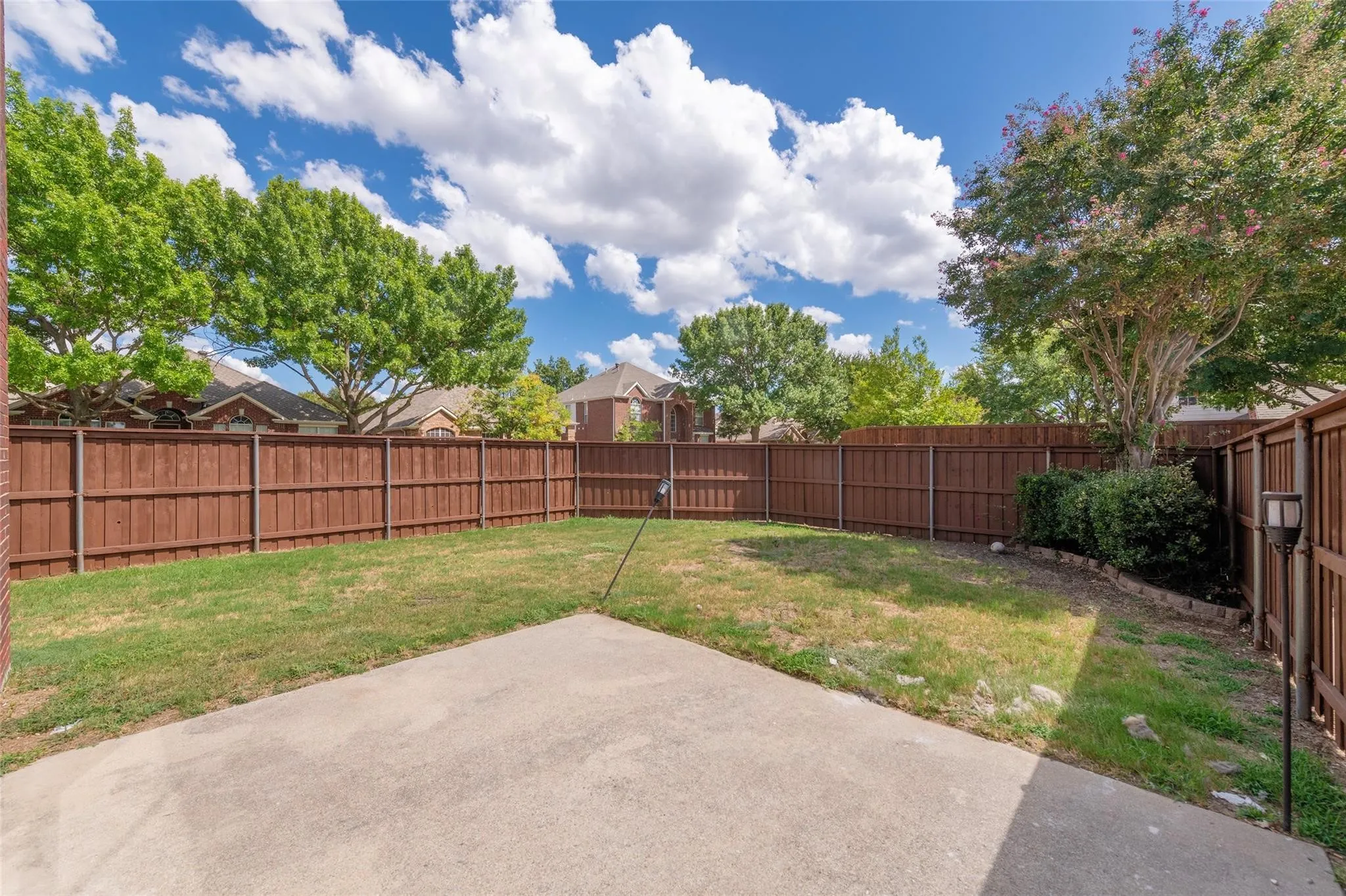 Expansive fenced backyard with a concrete patio, mature trees, and a landscaped perimeter
