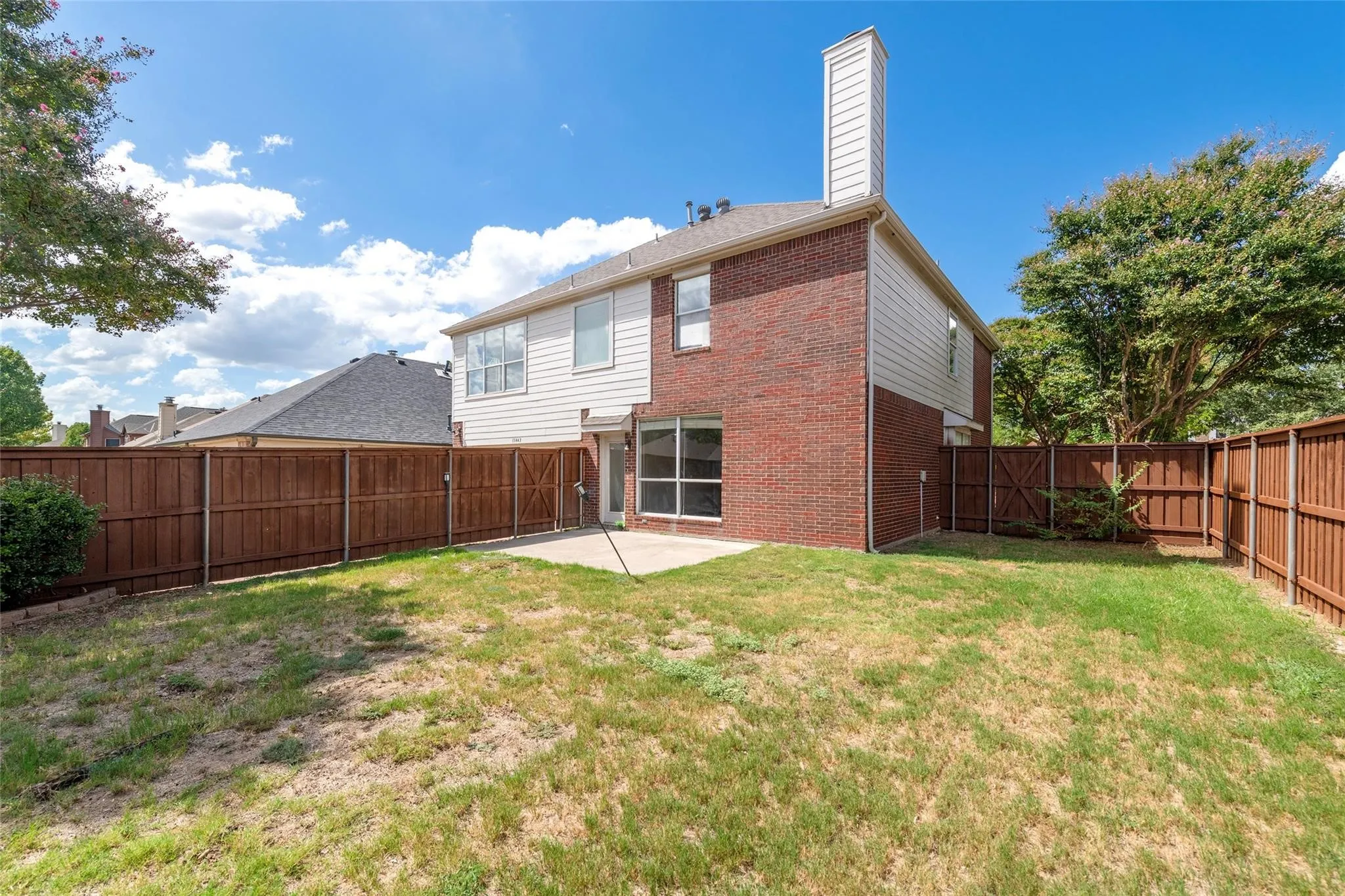 Backyard featuring a concrete patio, wood privacy fencing, and a two-story brick and siding exterior