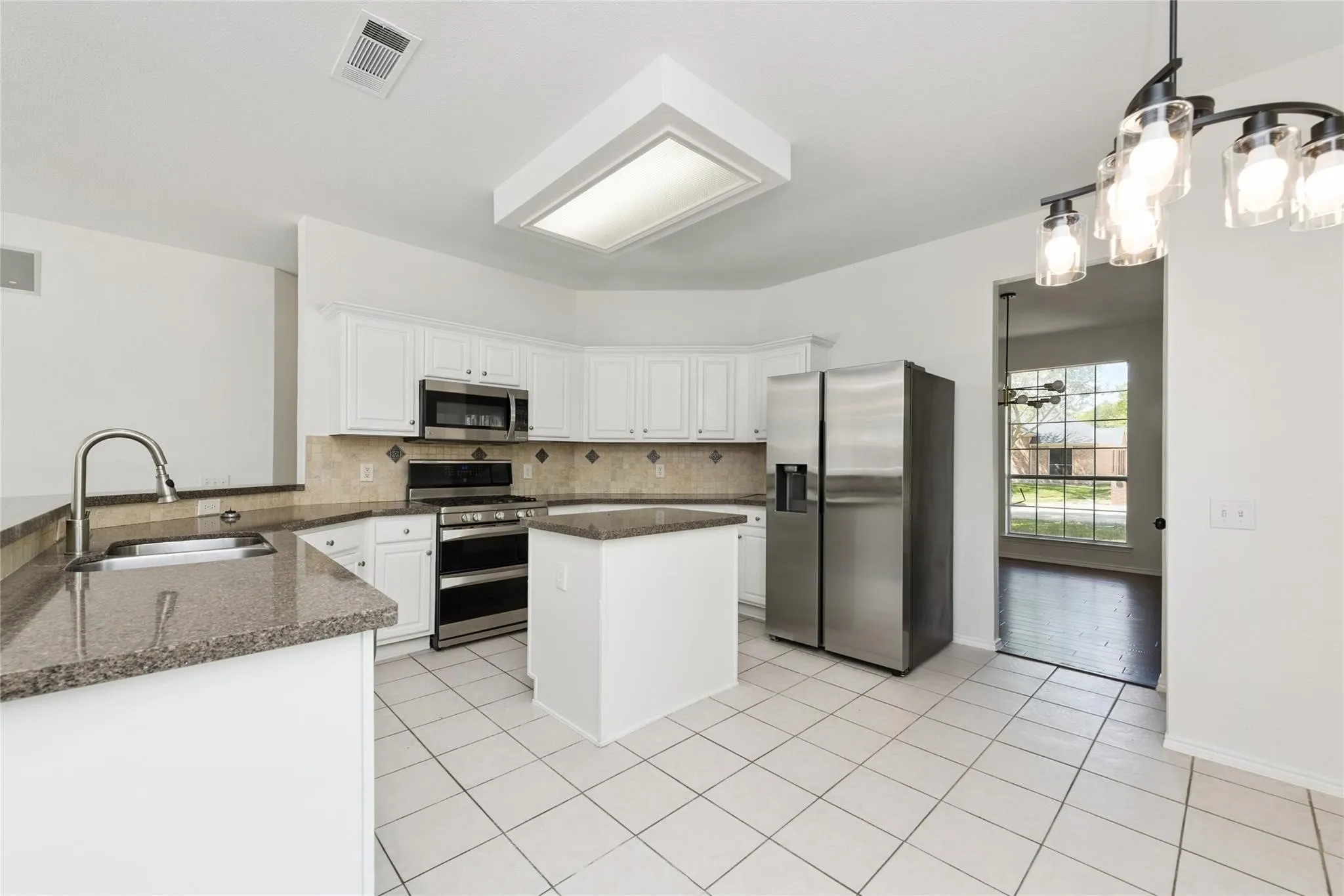 White cabinetry with stainless steel appliances, granite countertops, kitchen island, and tiled flooring