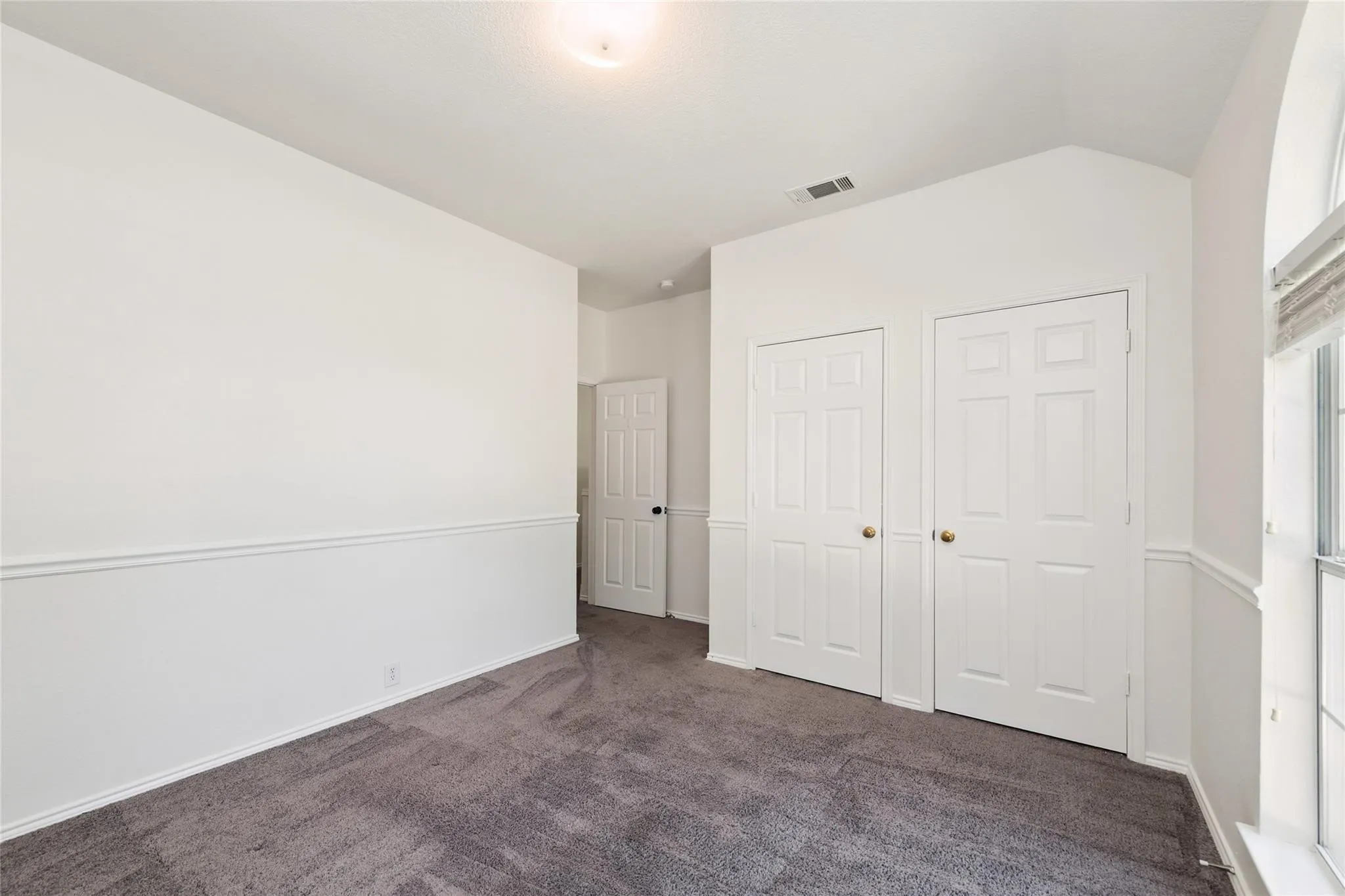 Plush gray carpet flooring, white paneled doors, wainscoting, and an arched window
