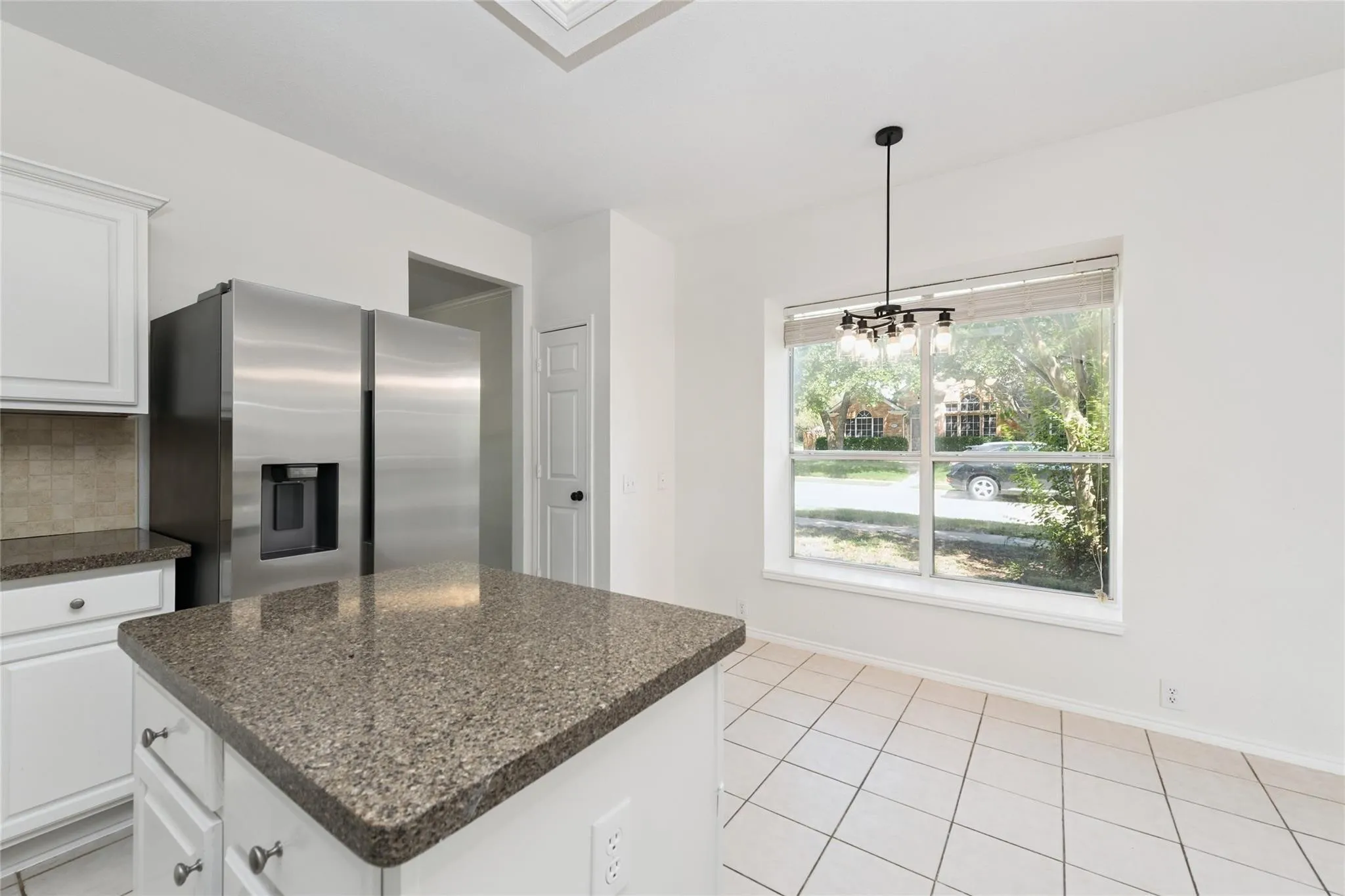 Kitchen featuring an island with stone countertops, white cabinetry, stainless steel refrigerator, tile backsplash, and tile flooring