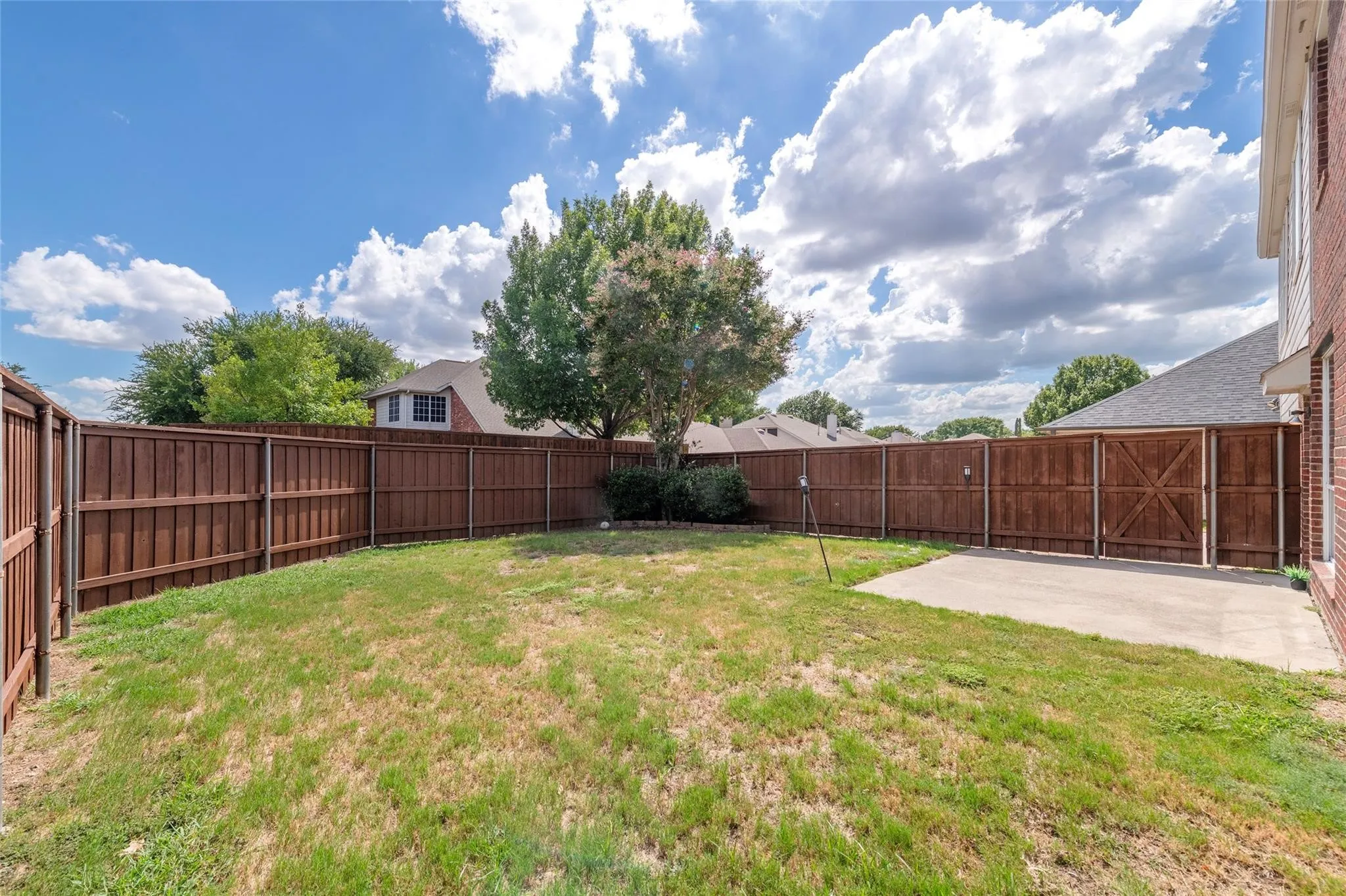 Expansive fenced backyard featuring a concrete patio, mature trees, and privacy fencing with gate access