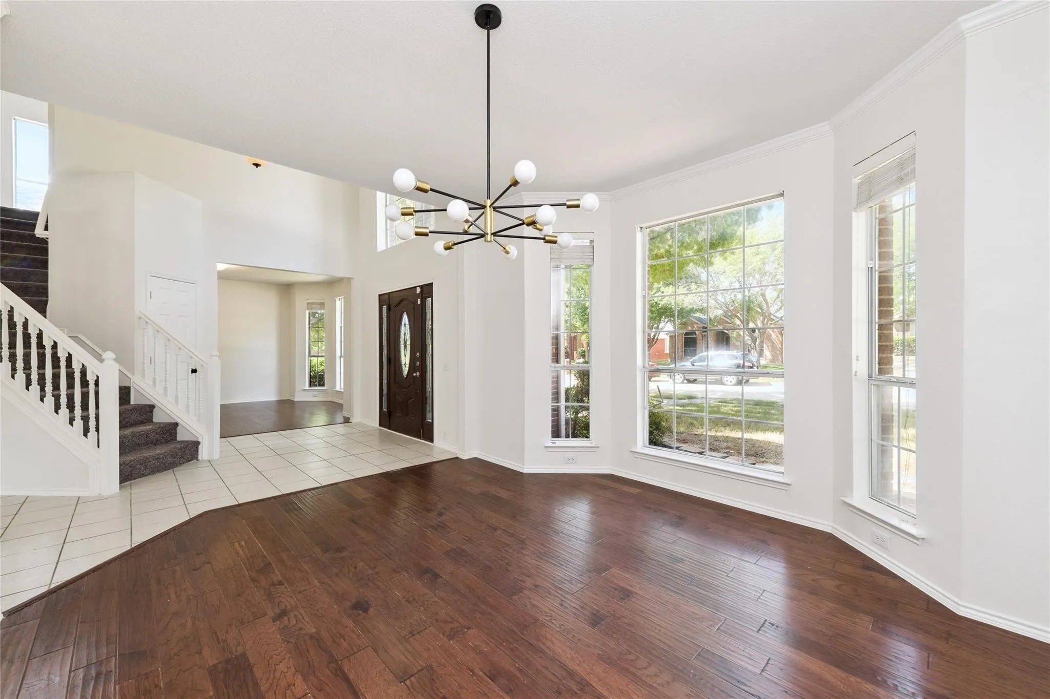 Hardwood flooring, bay windows, modern chandelier, two-story ceiling, and a grand staircase with white balusters