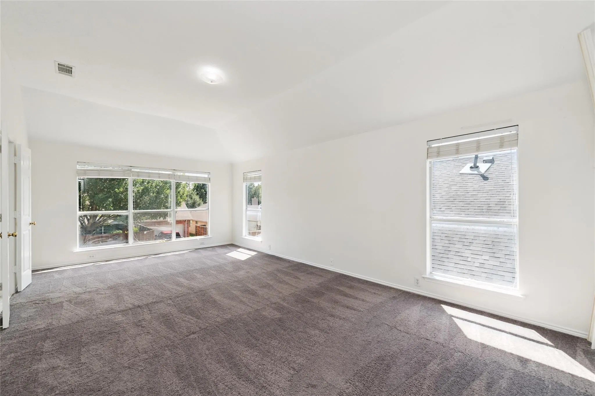 Vaulted ceiling with an overhead light fixture, light gray wall paint, and gray carpet flooring