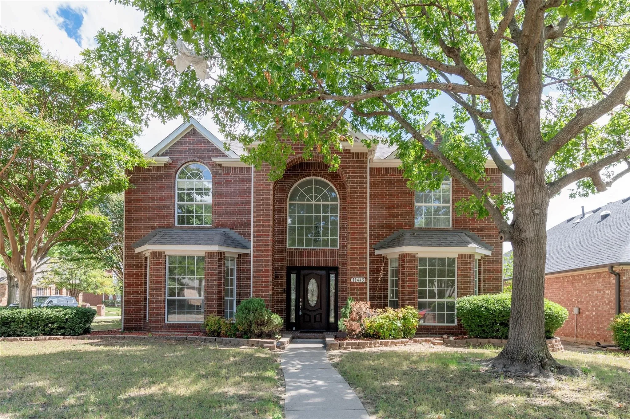 Brick exterior with arched and bay windows, a dark wood-finish entry door, and mature landscaping