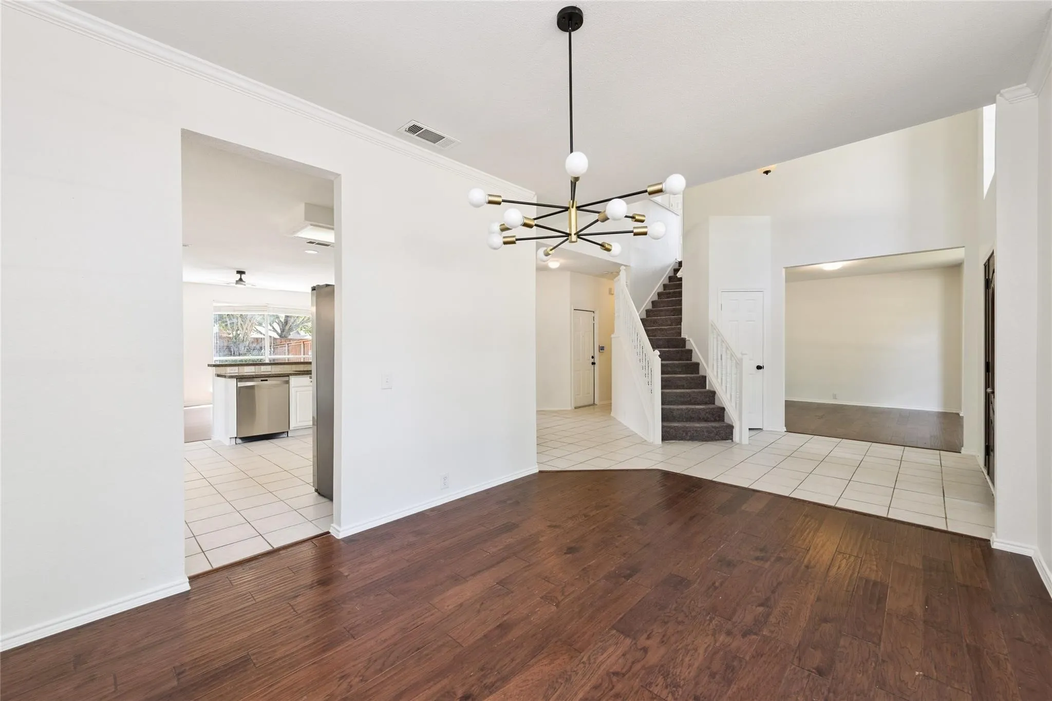 Dark wood-finish flooring, contemporary chandelier, white tile flooring, carpeted staircase, and stainless steel appliances