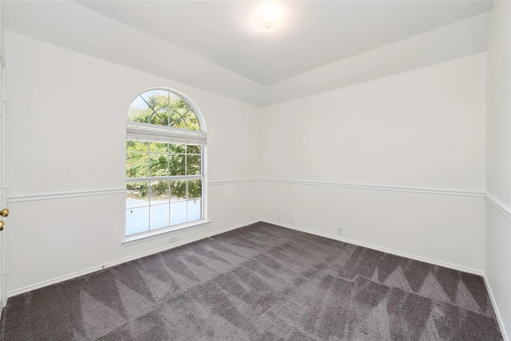Room featuring an arched window, white walls, and wainscoting
