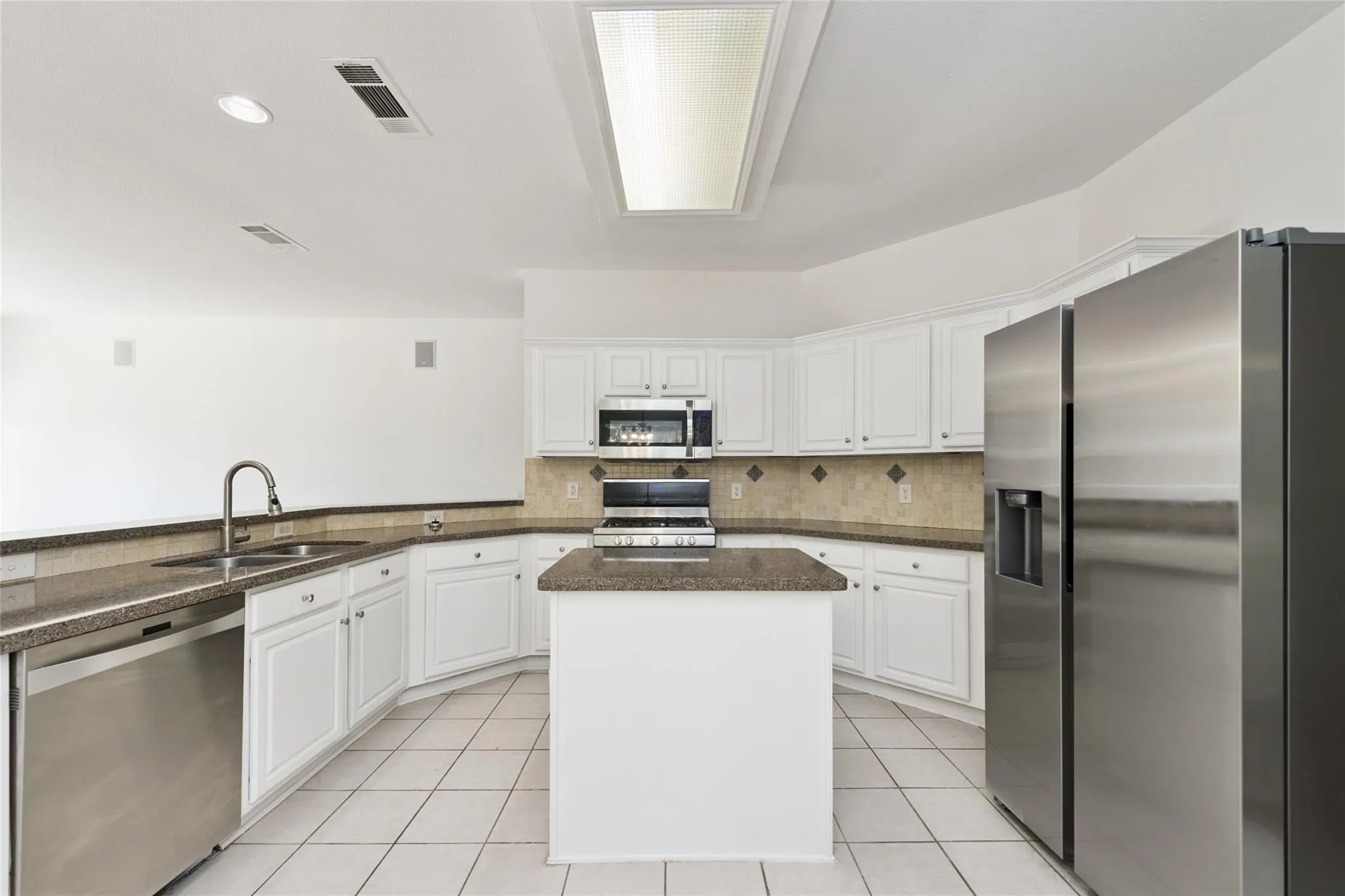 Kitchen featuring white cabinetry, stainless steel appliances, a center island, stone-finish countertops, and a tiled backsplash