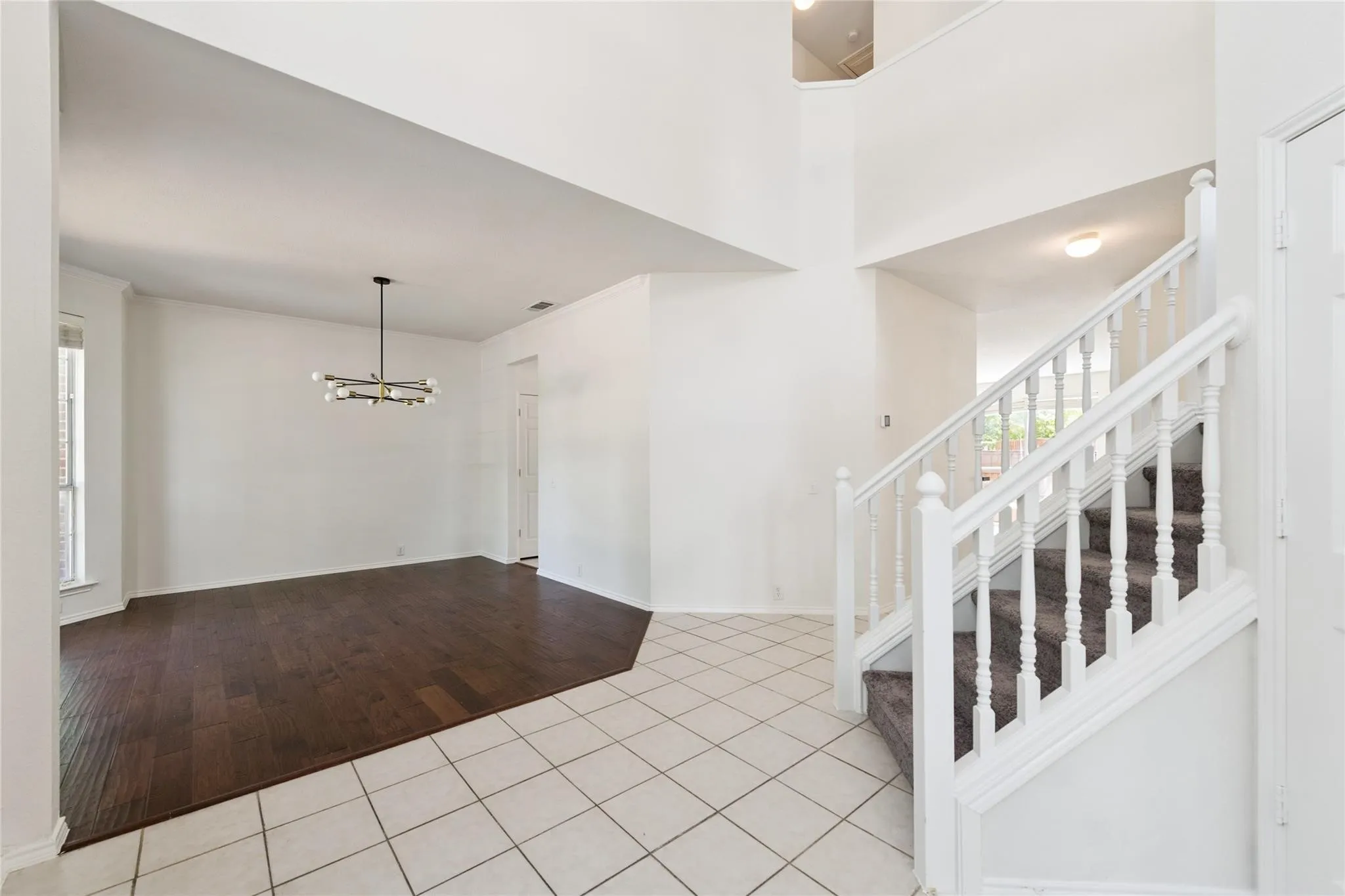 High ceilings featuring an open foyer, wood-finish flooring, a modern chandelier, and a carpeted staircase with white balusters