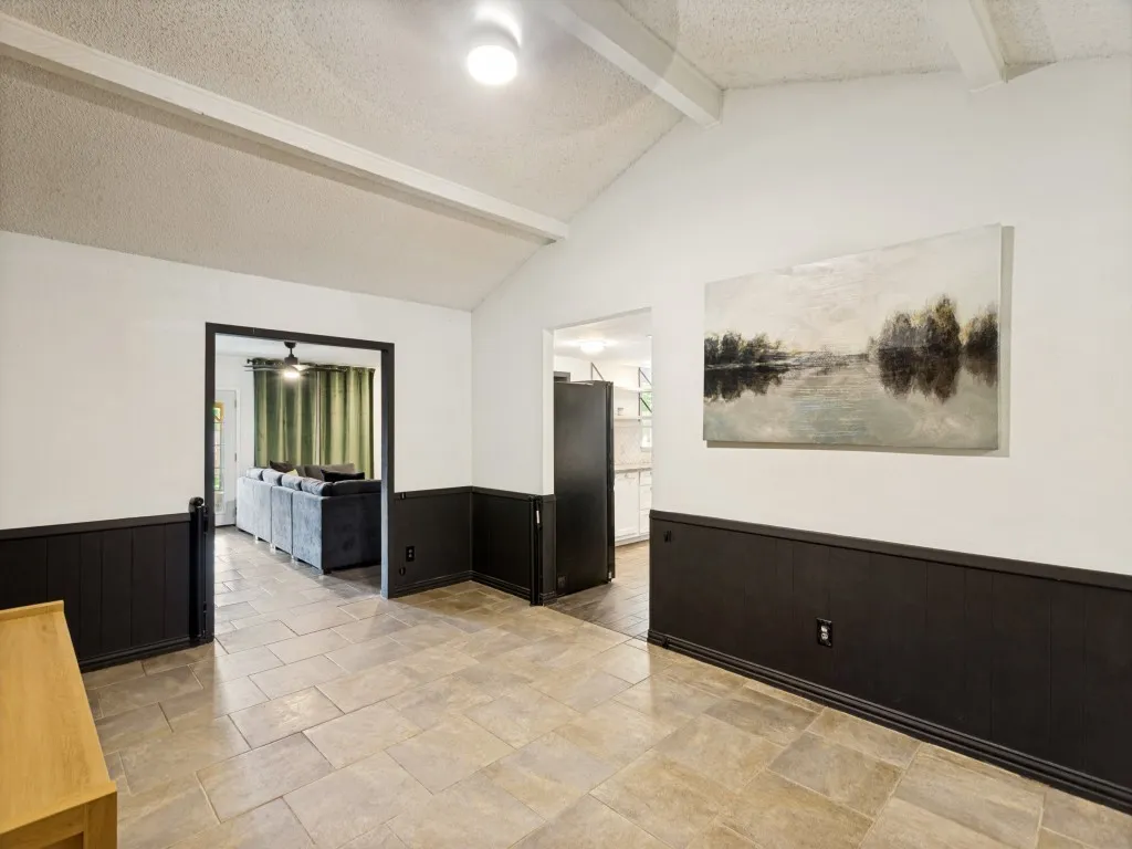 Vaulted ceiling with exposed beam, tile flooring, wainscoting, recessed lighting, and a defined doorway