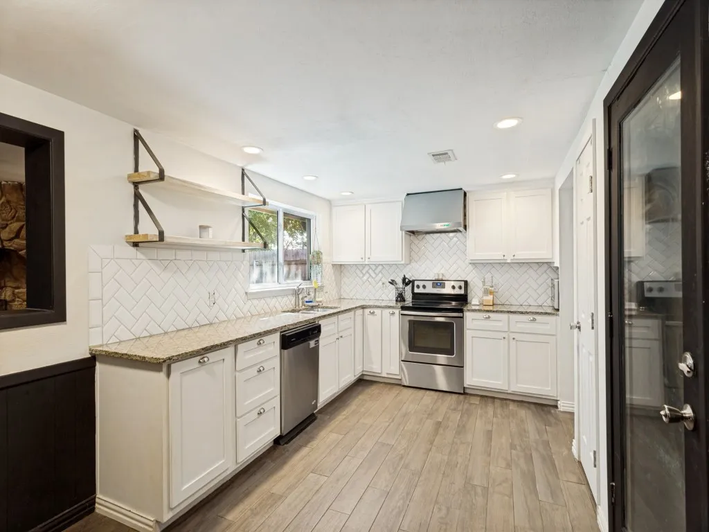 Modern kitchen featuring white cabinetry, stainless steel appliances, a herringbone tile backsplash, wood-finish flooring, and recessed lighting