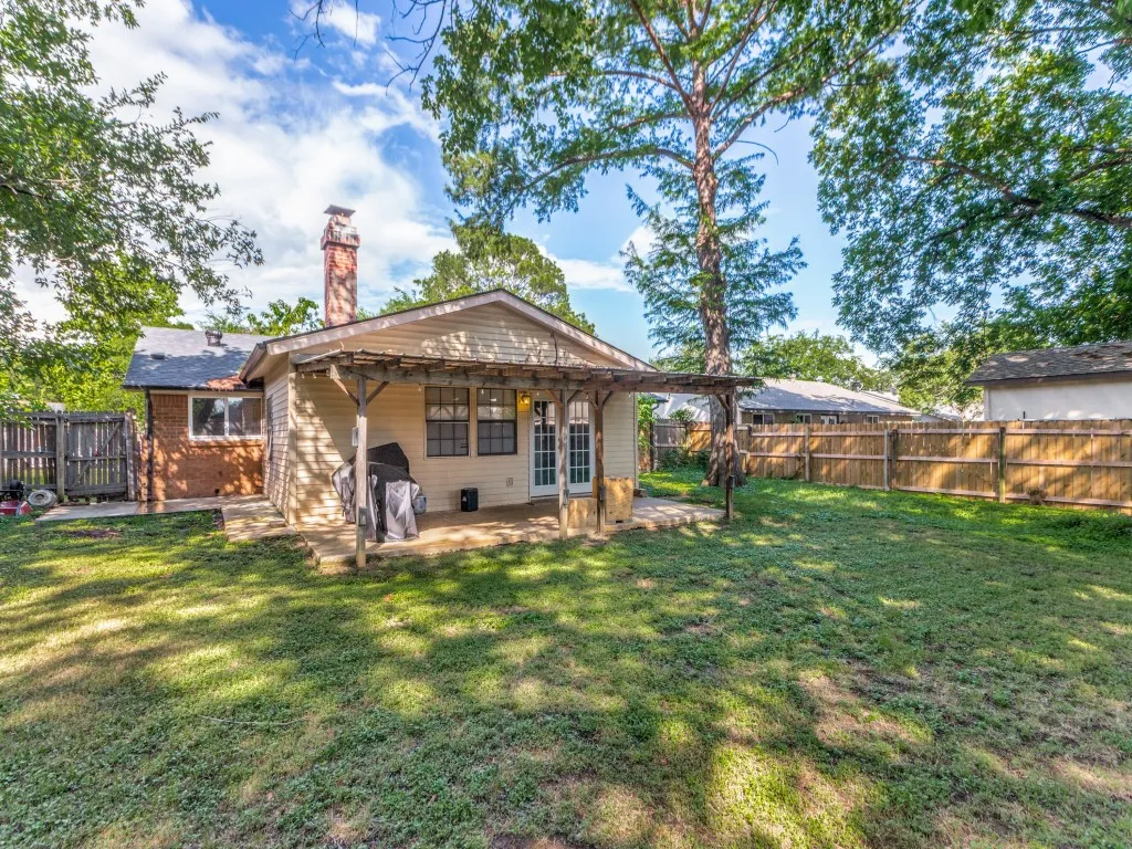 Expansive backyard with a manicured lawn, wood fencing, and a covered patio area