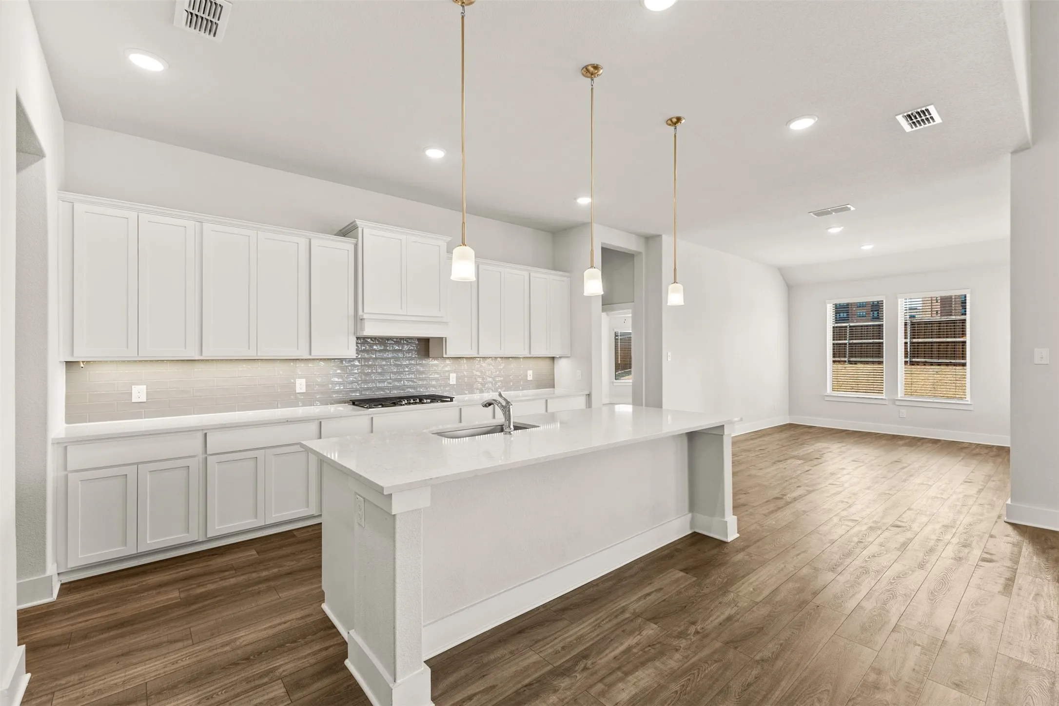 Open-concept kitchen featuring white shaker cabinetry, an expansive center island, pendant lighting, wood-finish flooring, and a tile backsplash