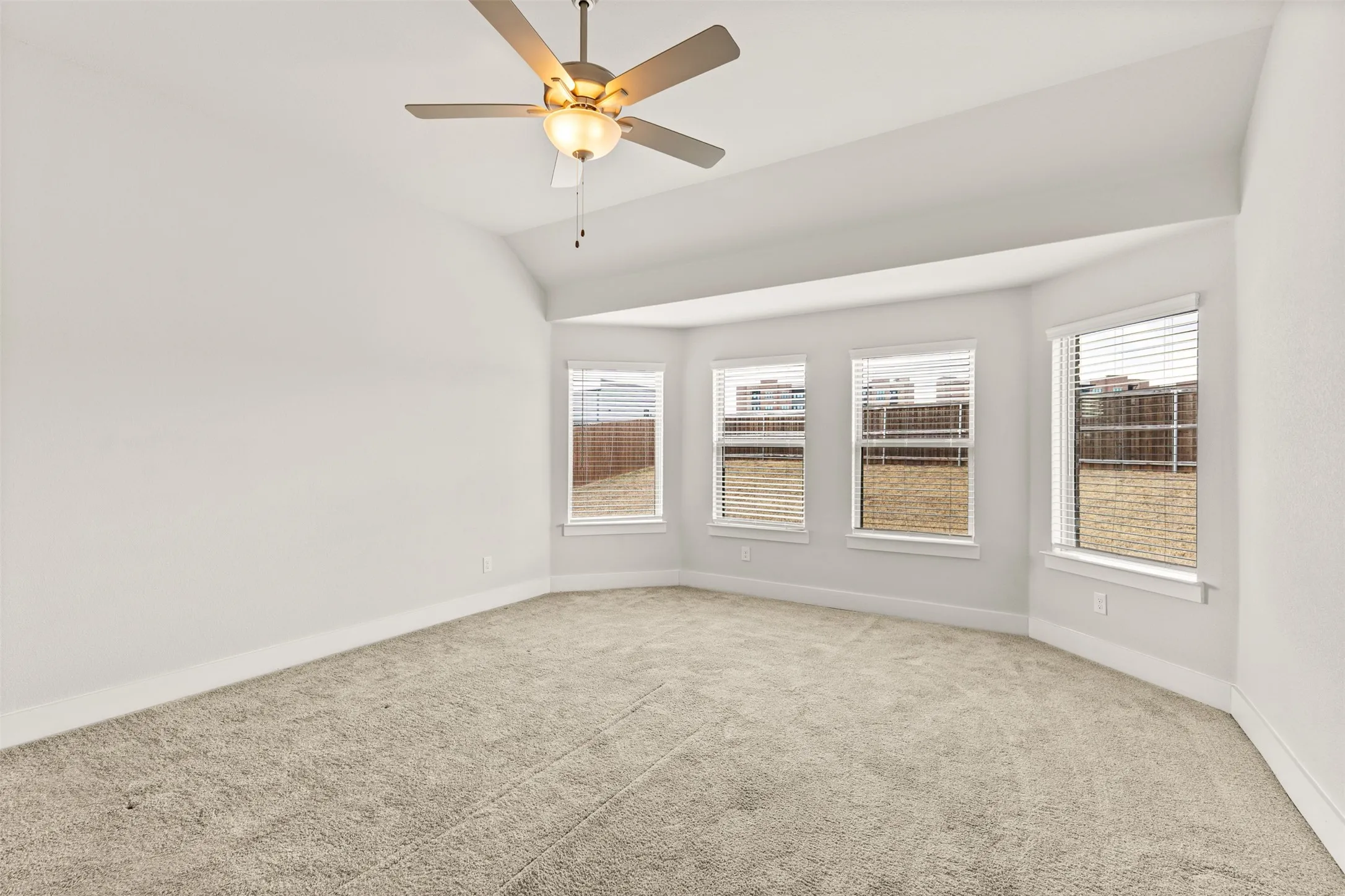 Vaulted ceiling with a ceiling fan, bay window configuration, multiple windows with blinds, and light-toned carpeting