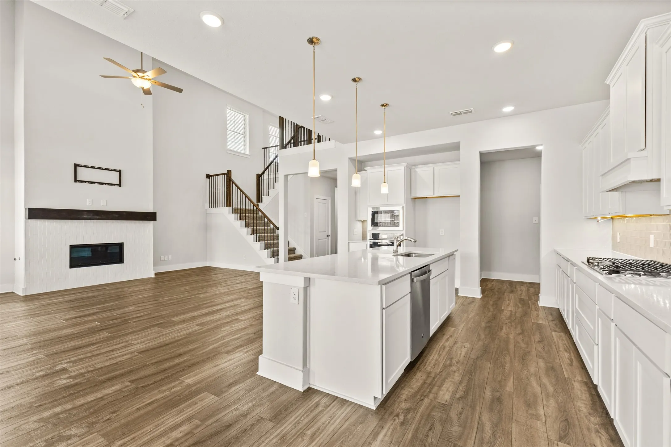 Open-concept layout featuring wood-finish flooring, a kitchen island with pendant lighting, white cabinetry, and stainless steel appliances