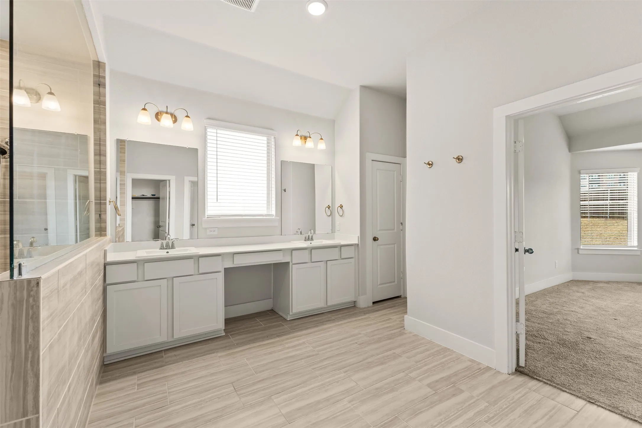 Dual vanity with integrated sinks, tiled flooring, glass-enclosed shower, and a built-in dressing table