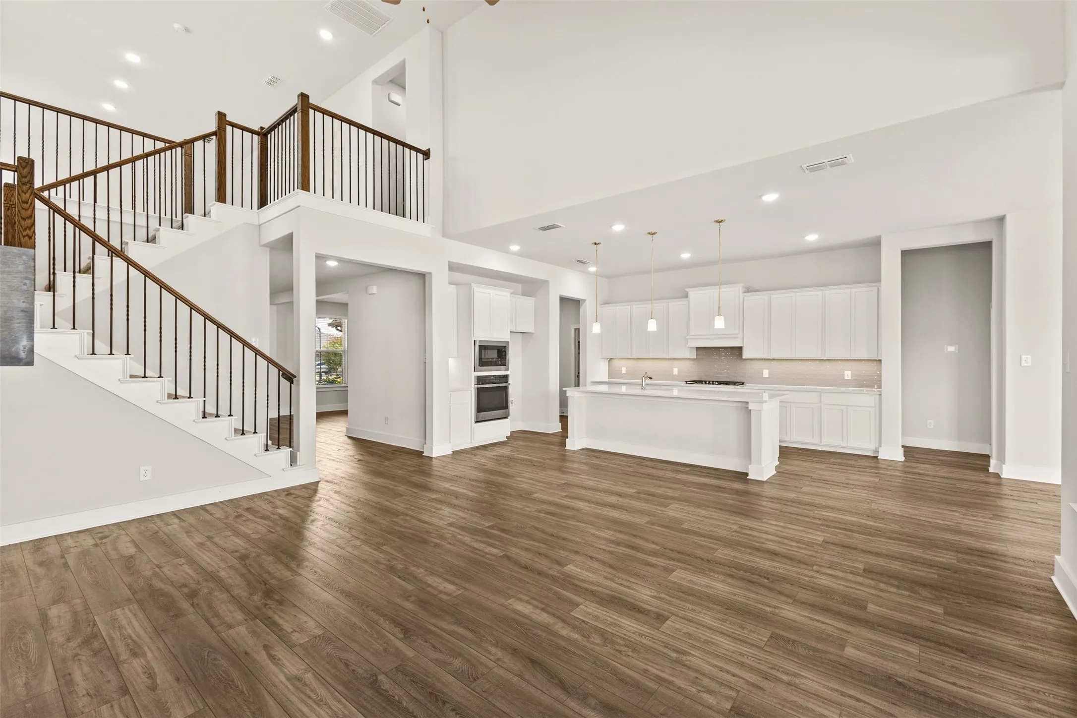 Open-concept living space featuring wood-finish flooring, a two-story ceiling, a contemporary kitchen with white cabinetry, a large kitchen island, and a staircase with wood and wrought iron balusters
