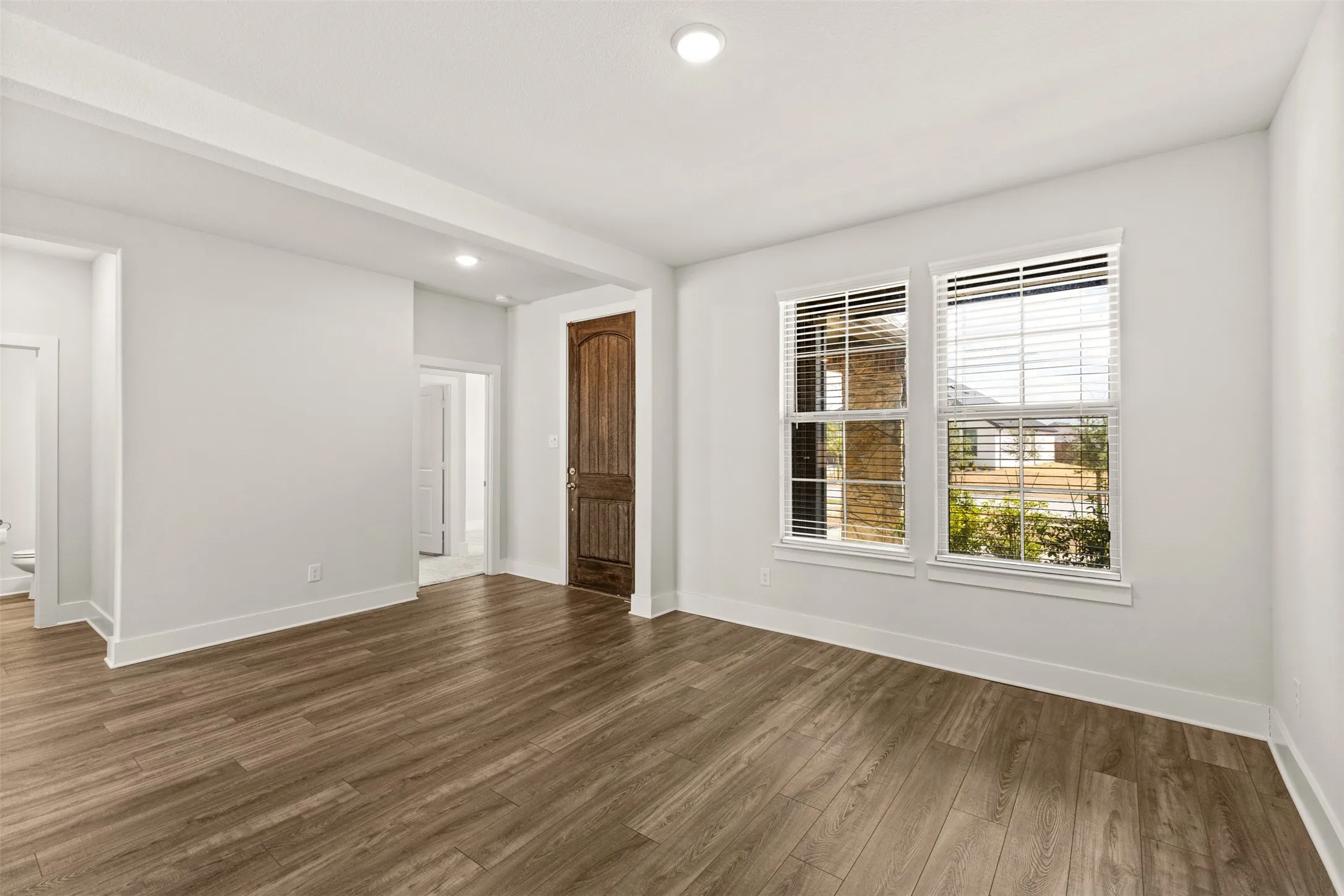 Wood-finish flooring, two large windows with blinds, recessed lighting, and a paneled wood door