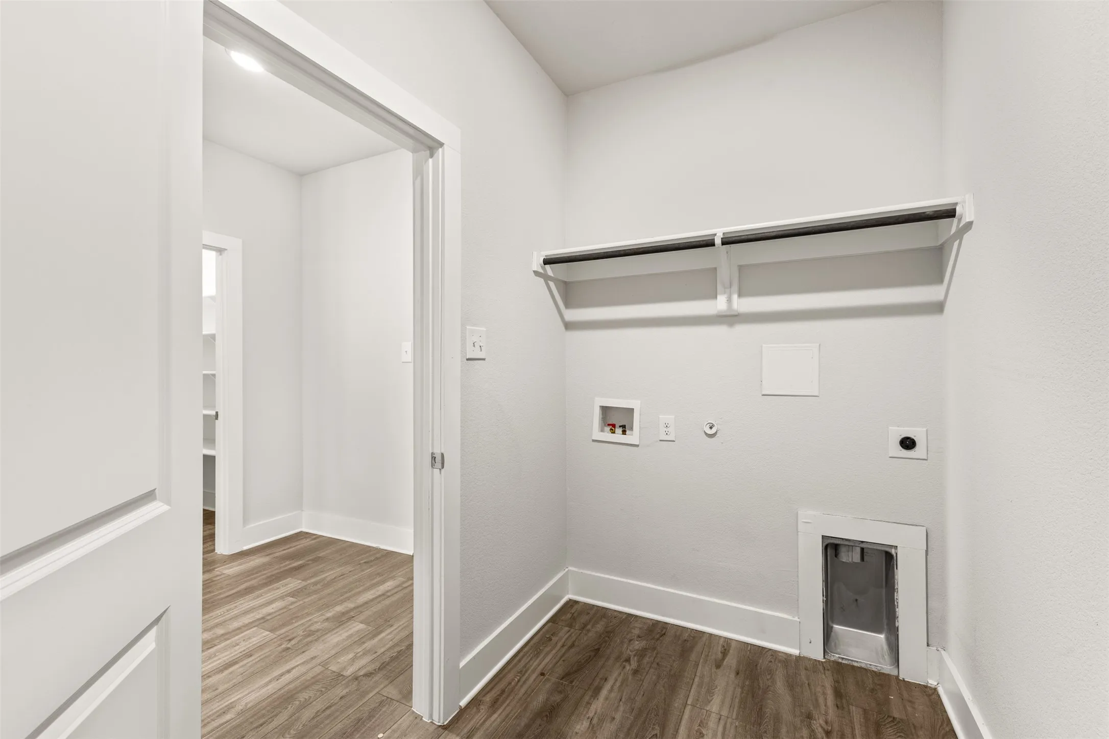 Dedicated laundry area with wood-finish flooring, white walls, and built-in shelving