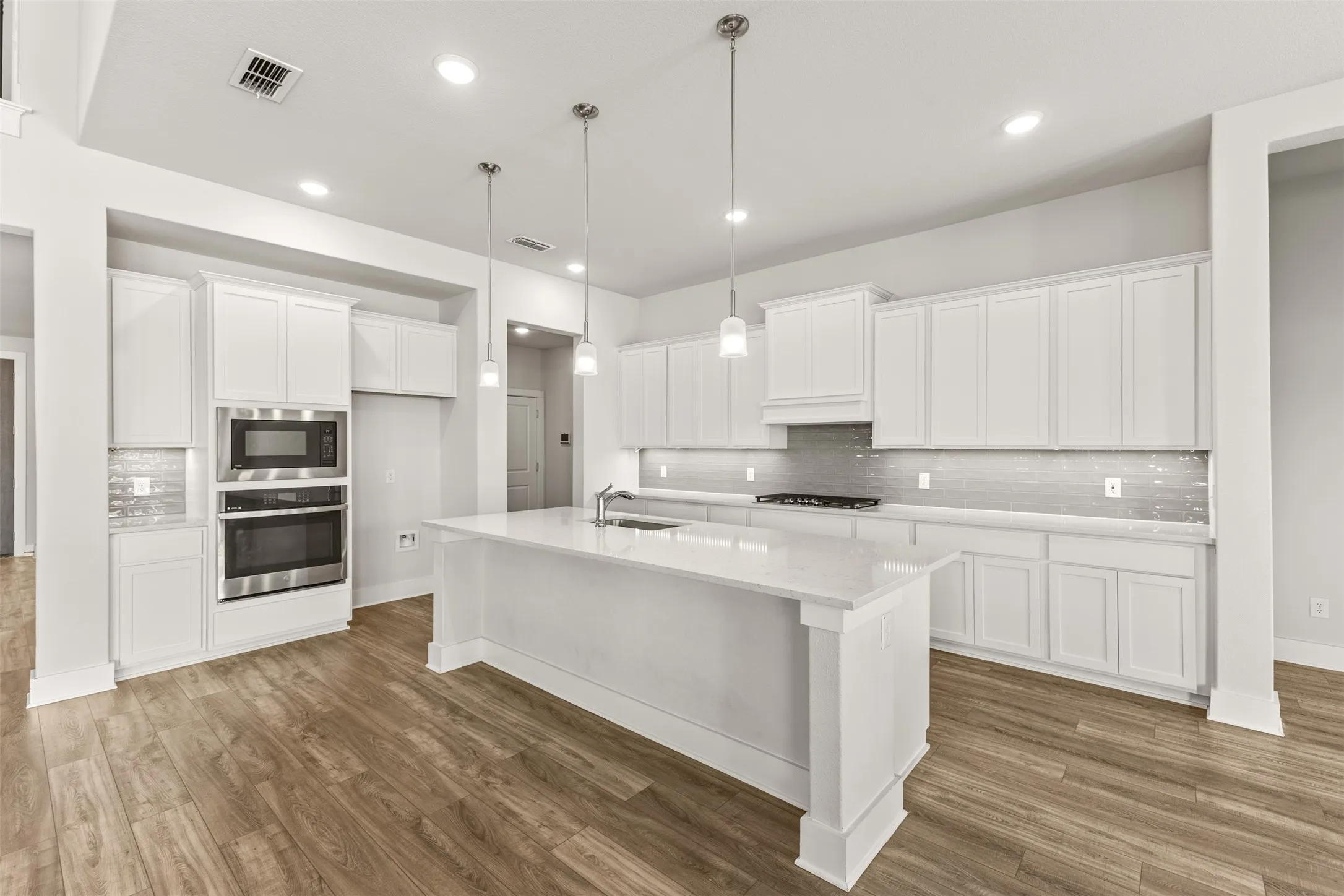 Spacious kitchen featuring an expansive island, white cabinetry, integrated stainless steel appliances, a tiled backsplash, and wood-finish flooring