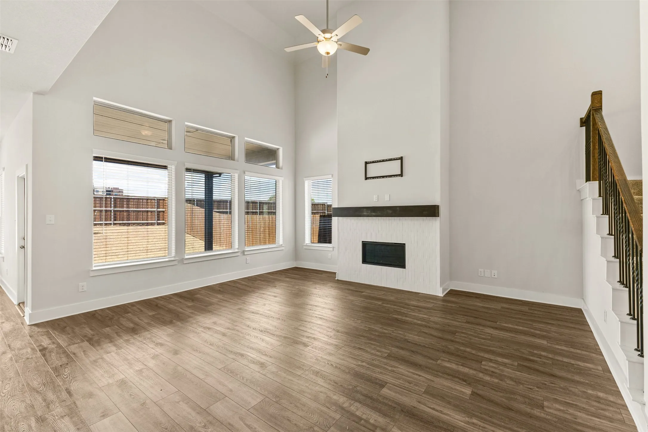 Spacious living area featuring high ceilings, wood-finish flooring, a contemporary fireplace with a wood mantle, and an open staircase with iron balusters