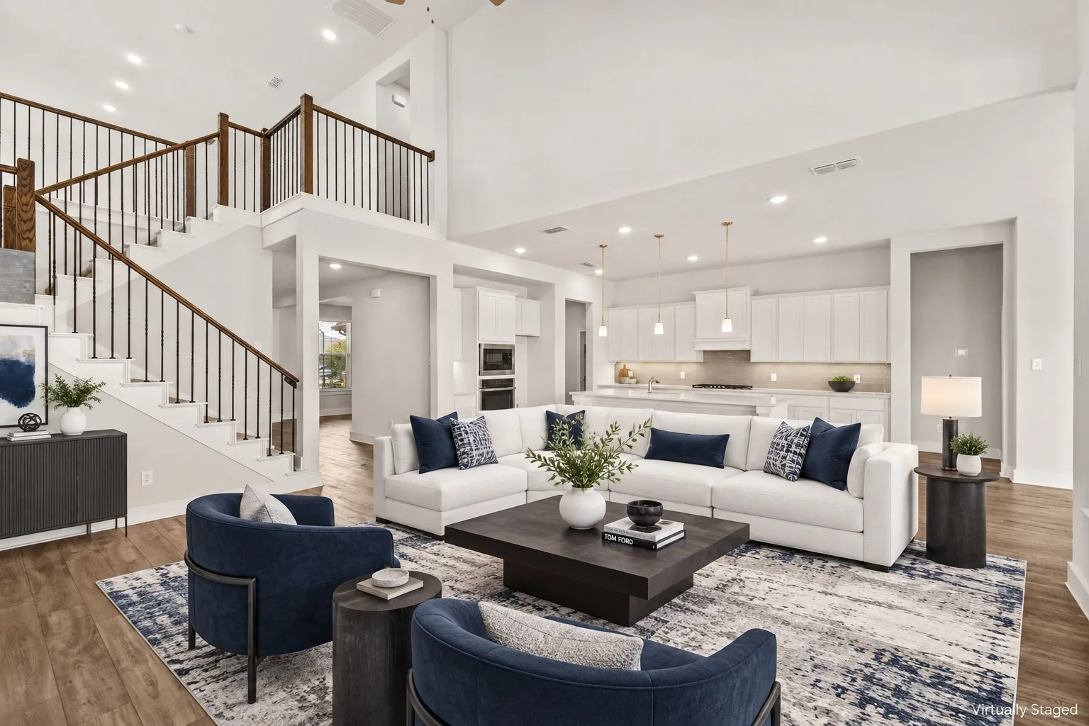 Expansive living area featuring soaring ceilings, a dual-level staircase with wrought iron balusters, wood-finish flooring, and a modern open-concept kitchen with integrated appliances