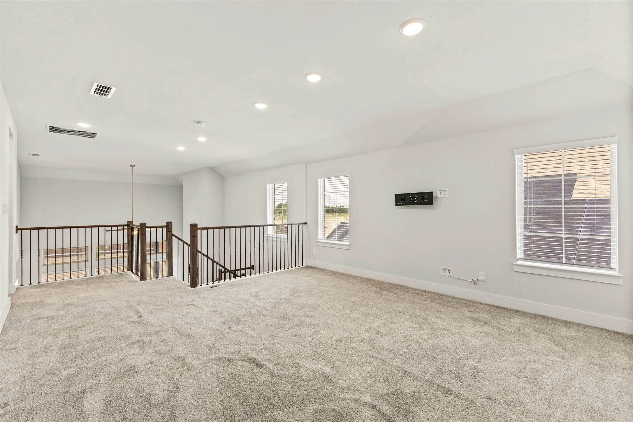 Spacious loft area featuring light gray carpeting, recessed ceiling lighting, and multiple windows