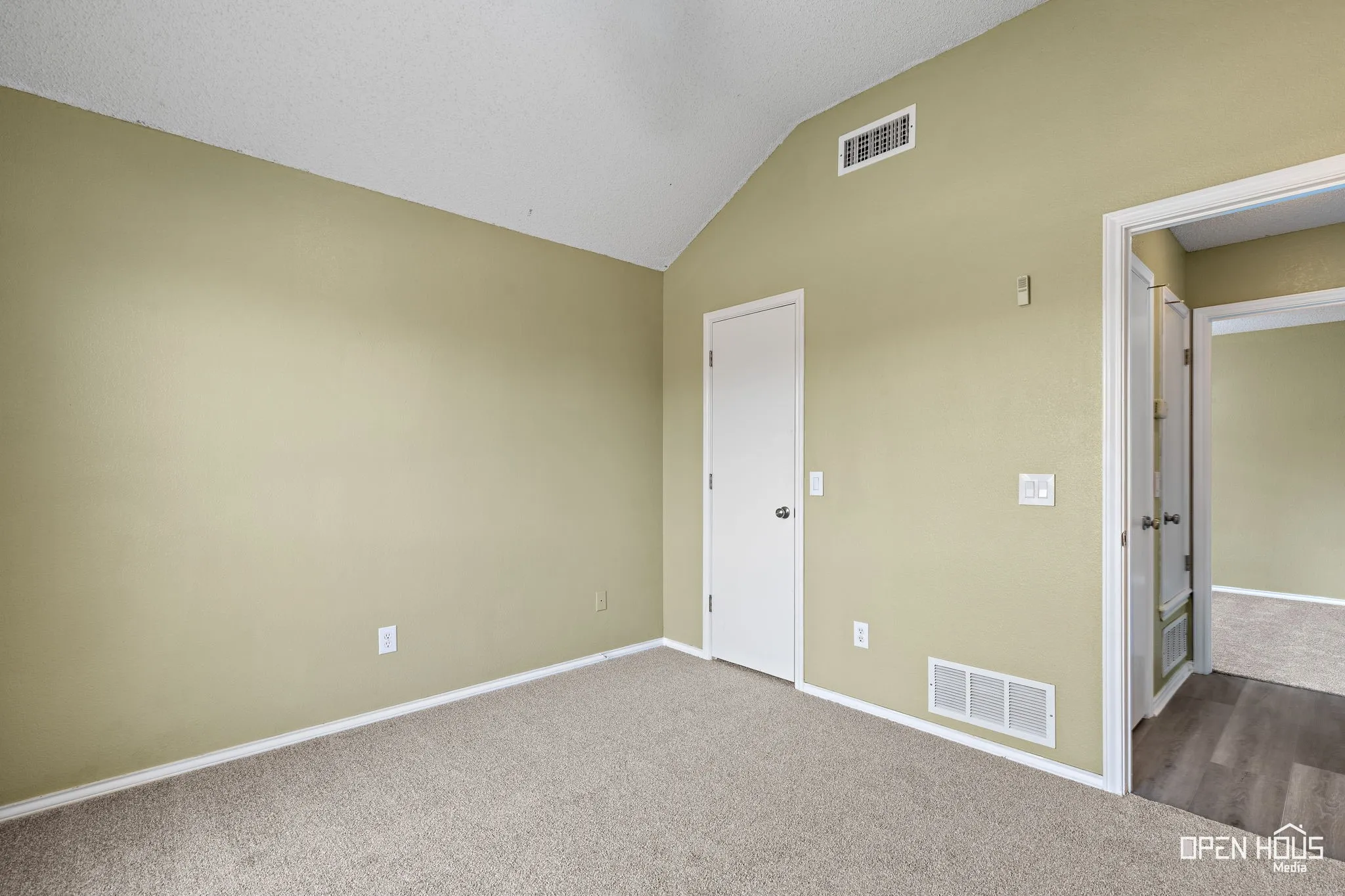 Vaulted ceiling with an overhead vent, light-colored carpeting, a white door, and a doorway with wood-finish flooring