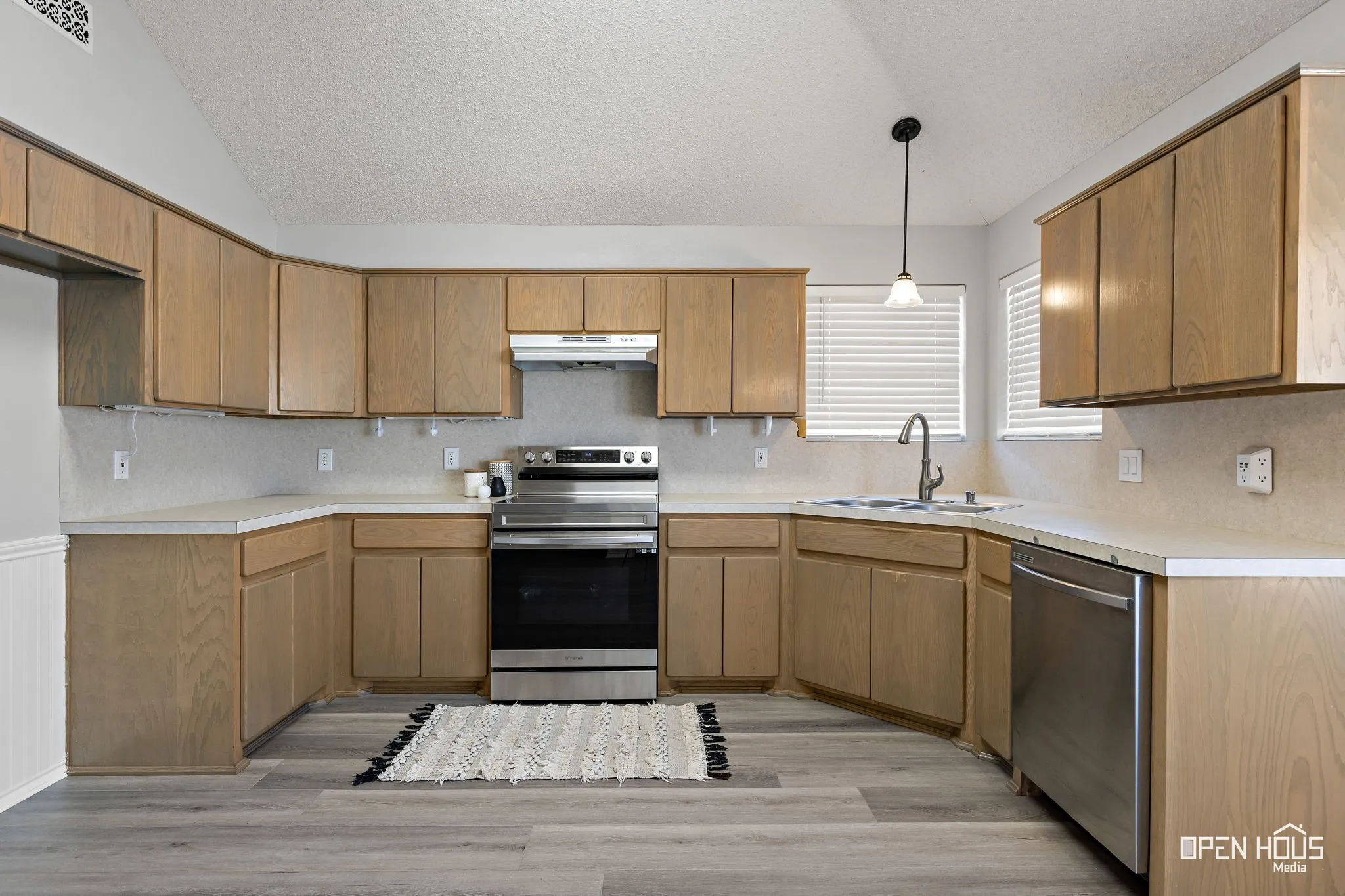 Kitchen featuring wood-finish cabinetry, stainless steel range, stainless steel dishwasher, and a single basin sink with a gooseneck faucet