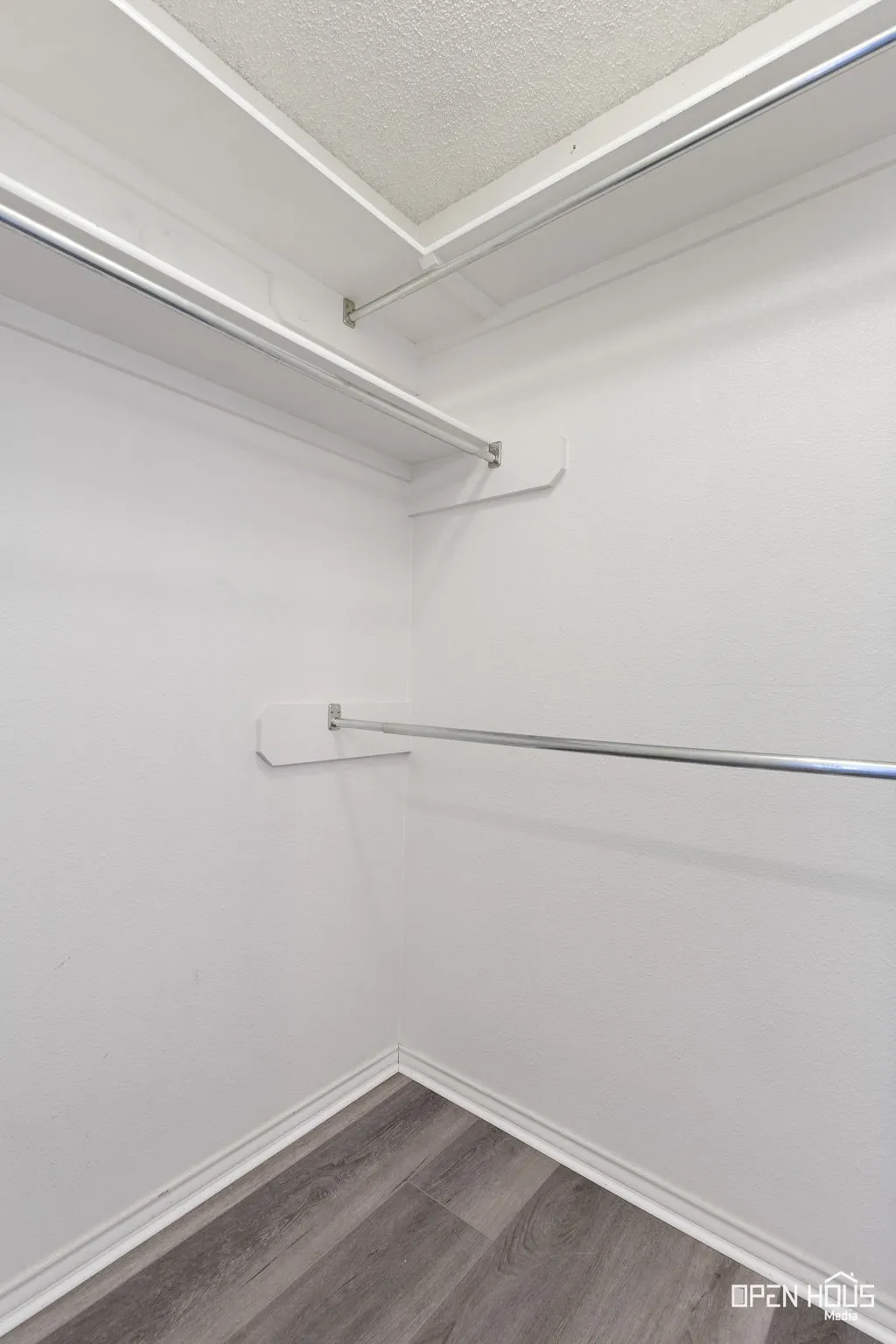 Wood-finish flooring with white baseboards, white walls, and built-in closet shelving and hanging rods