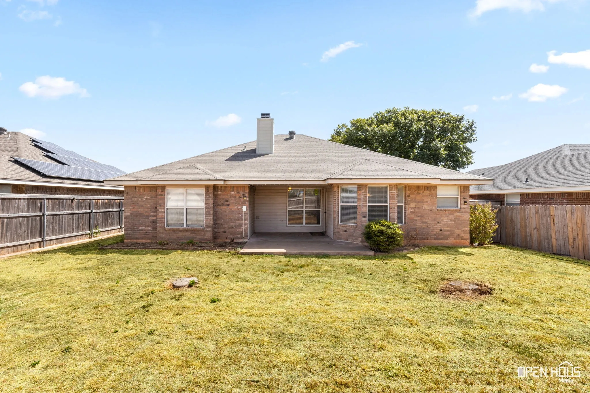 Rear exterior featuring a brick facade, shingled roof, and a concrete patio