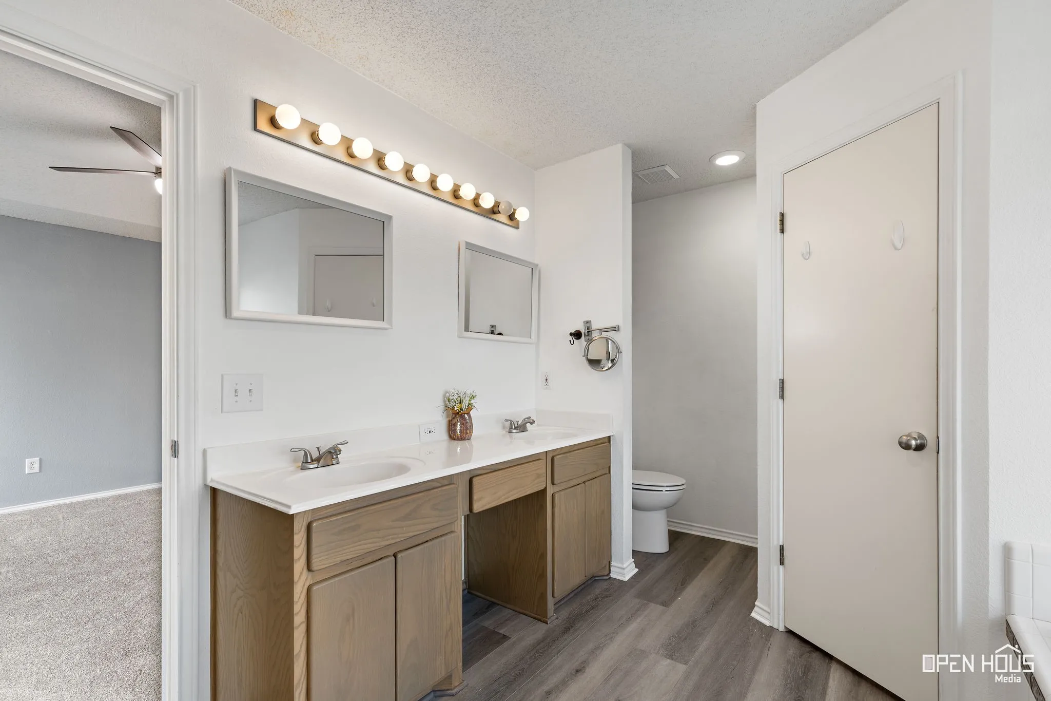 Dual vanity with white countertops, wood-finish cabinetry, and contemporary lighting