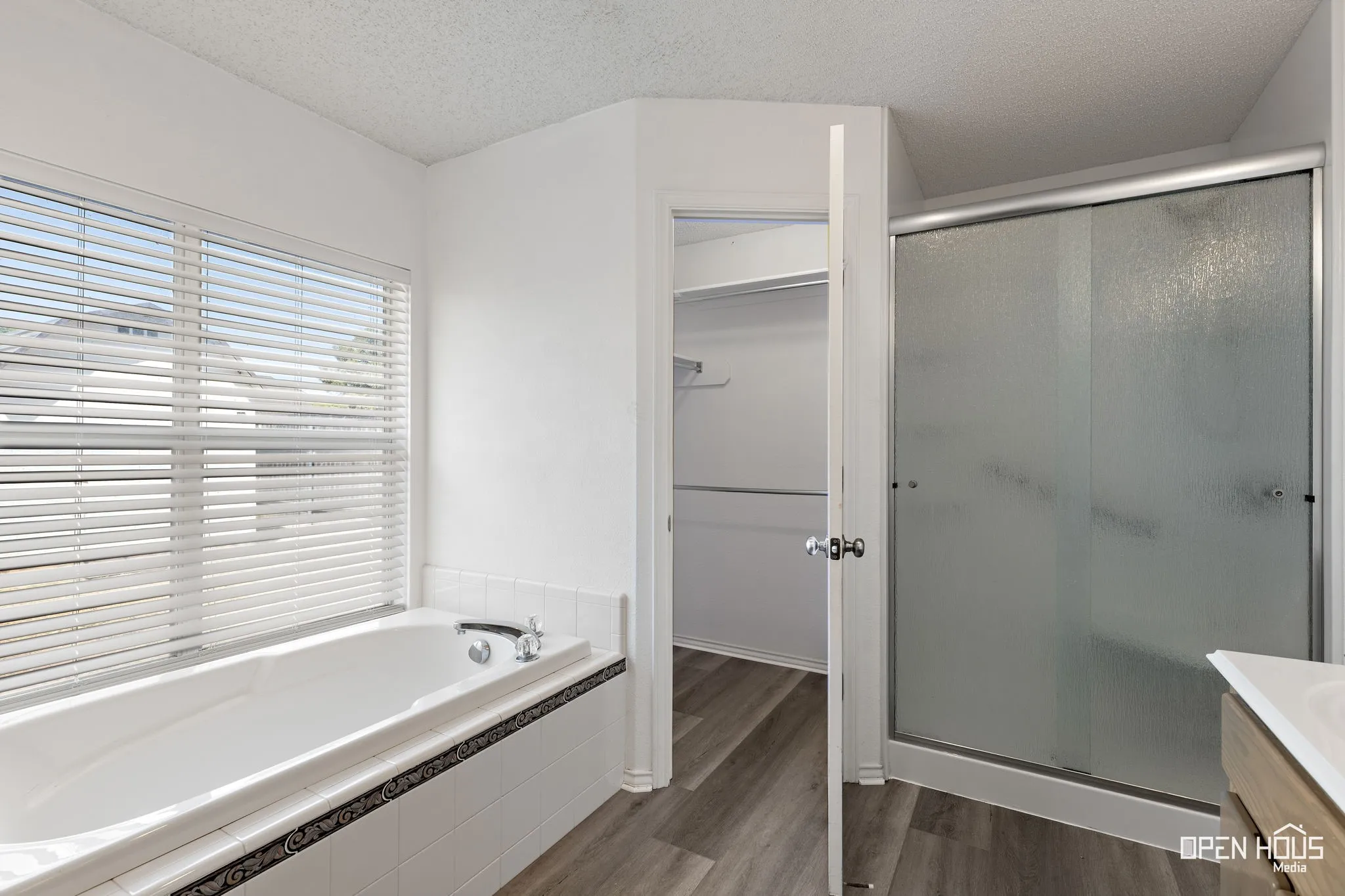 Built-in bathtub with tiled surround, wood-finish flooring, and a frosted glass shower enclosure