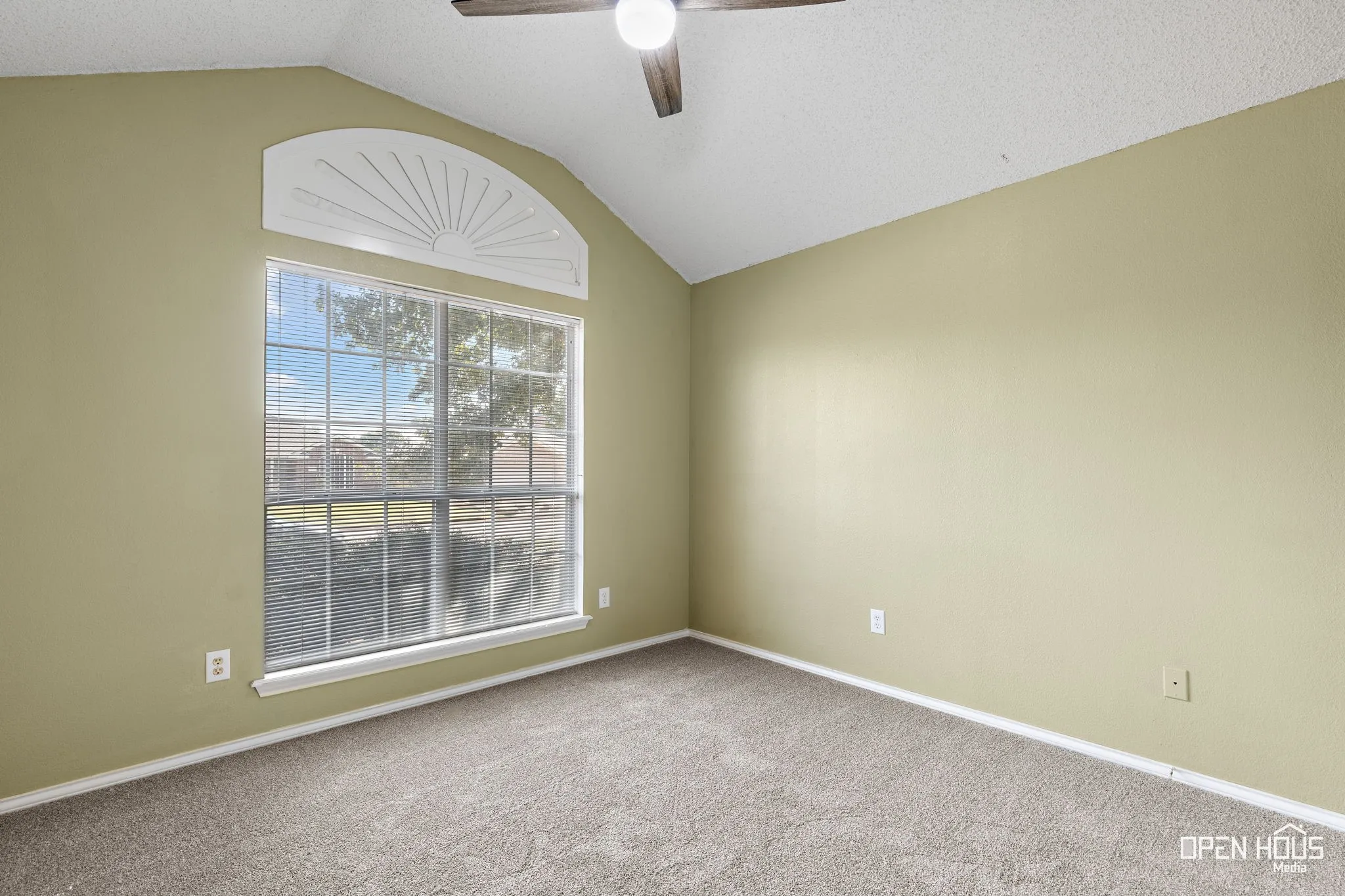 Vaulted ceiling, arched window with decorative molding, ceiling fan, and carpeted flooring