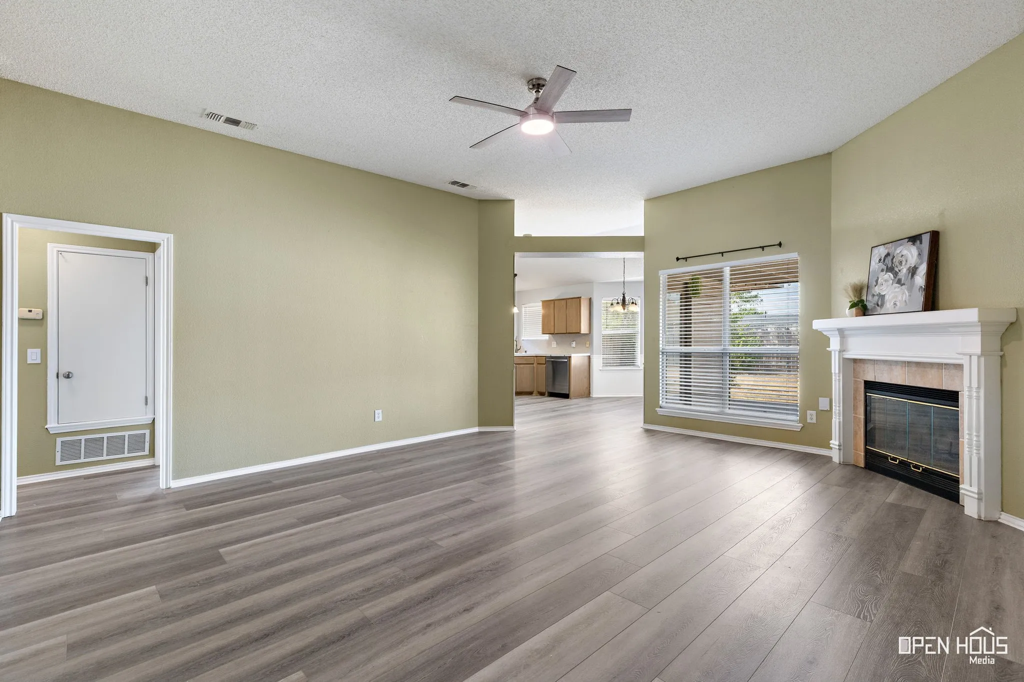 Wood-finish flooring throughout, featuring a fireplace with a white mantel, and a ceiling fan
