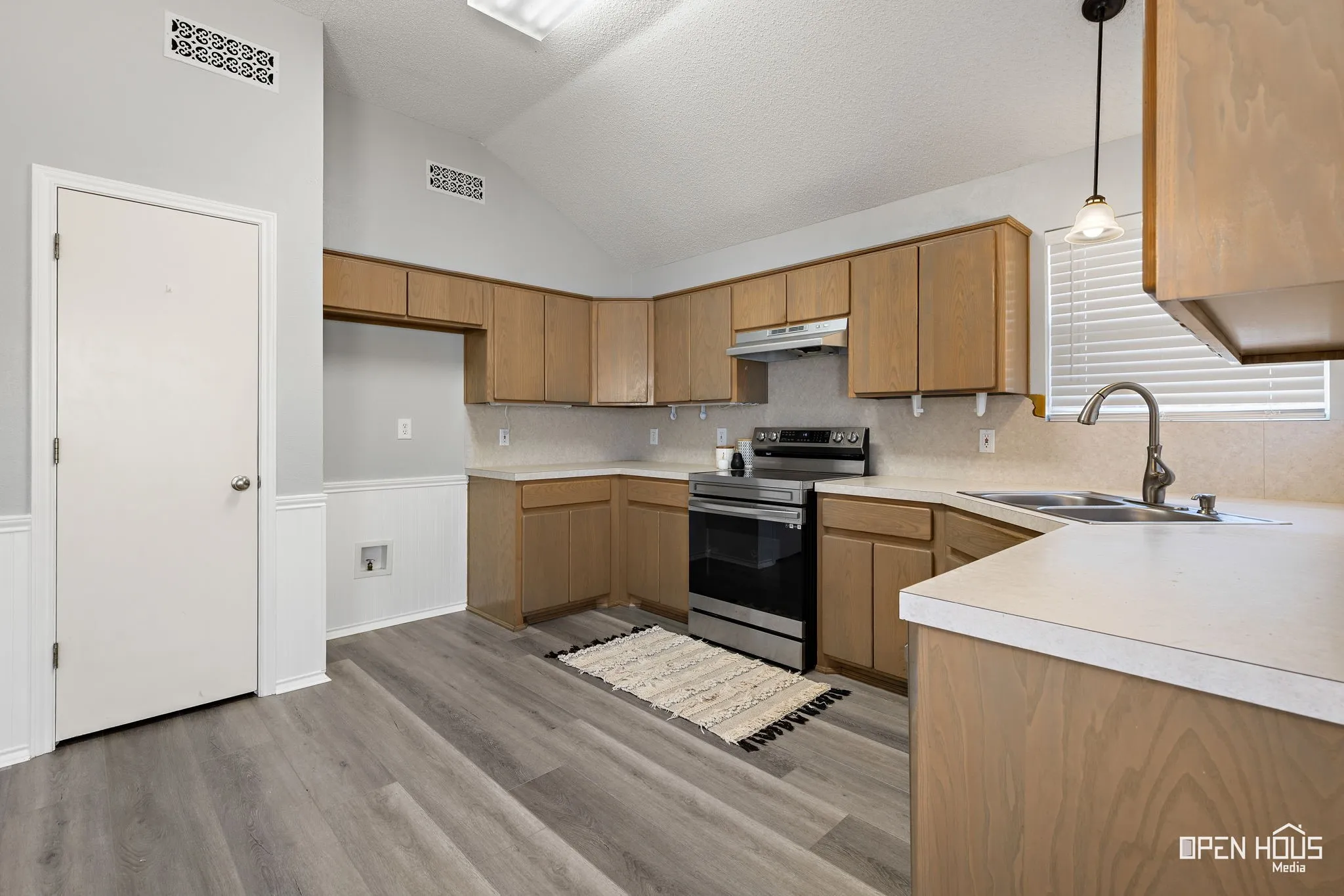 Kitchen featuring wood-finish cabinetry, light-toned countertops, stainless steel appliances, a corner sink, and vaulted ceilings