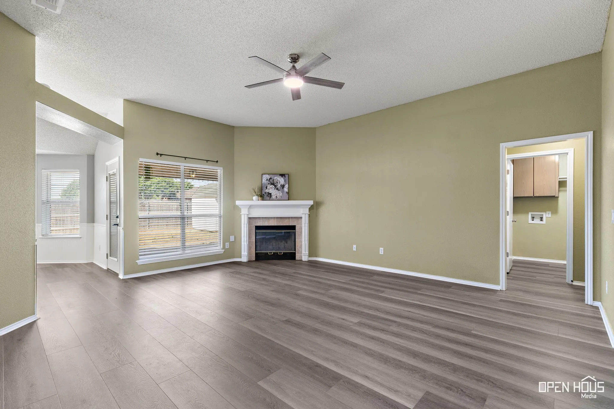 Wood-finish flooring, ceiling fan, fireplace with mantel, and large windows with blinds