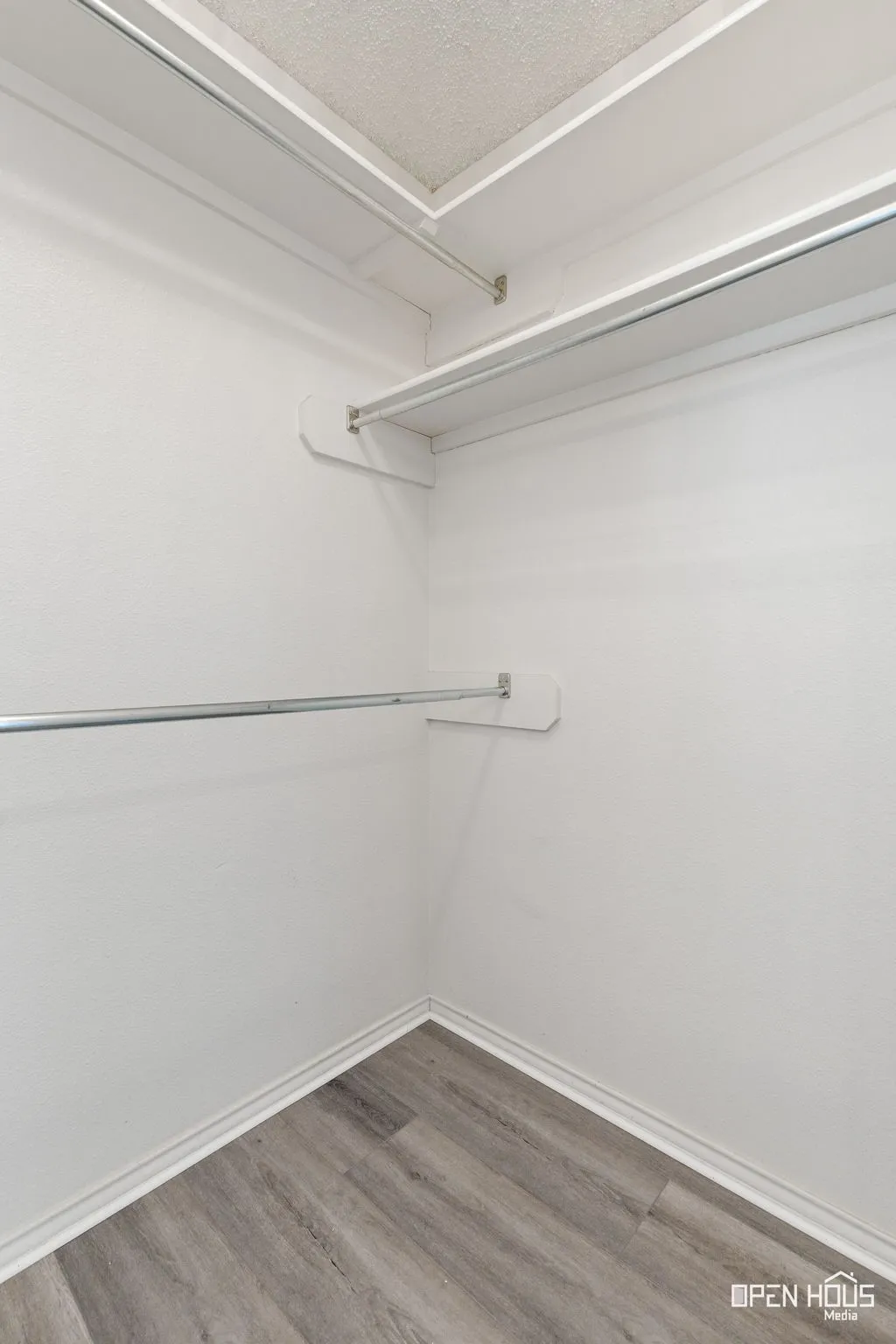 Interior closet with wood-finish flooring, white walls, and built-in shelving with hanging rods