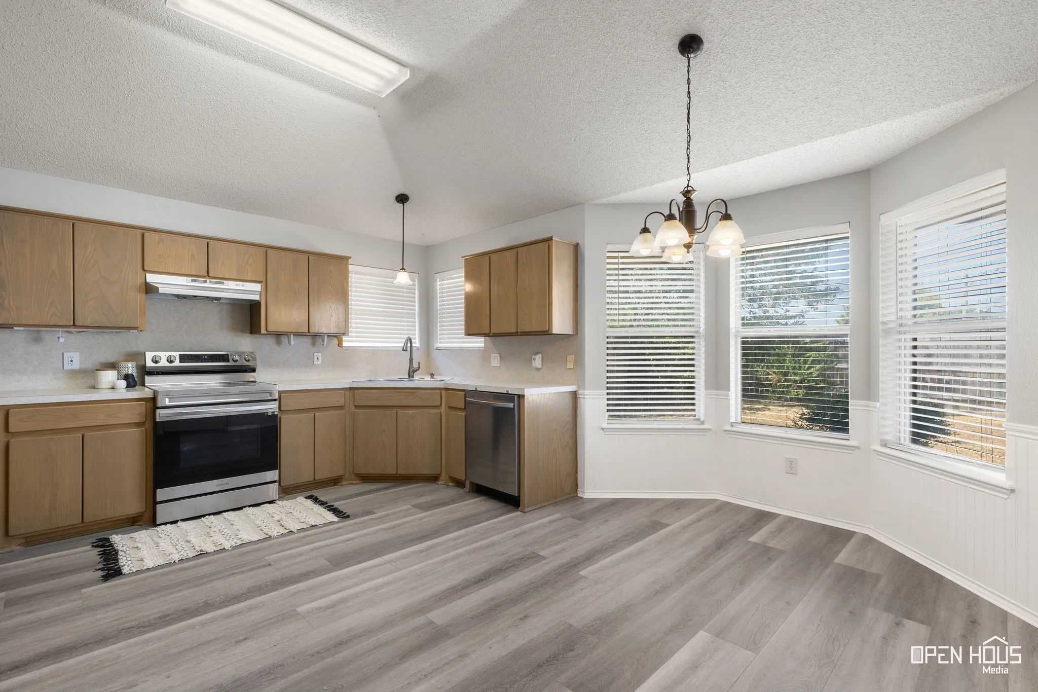 Spacious kitchen featuring light wood cabinetry, stainless steel appliances, wood-finish flooring, and a bay window dining area with a multi-light chandelier