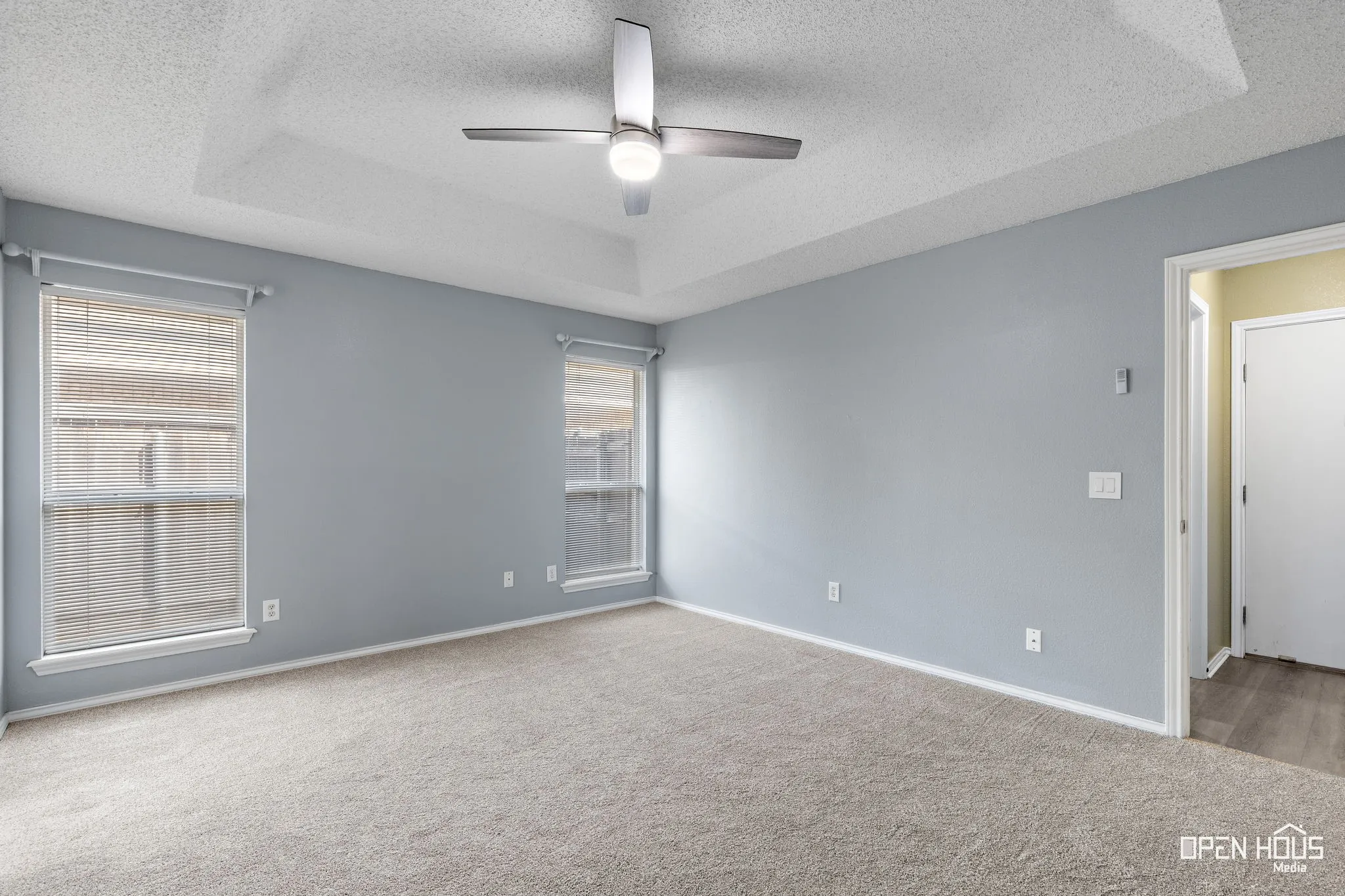 Tray ceiling with a ceiling fan, two windows with blinds, and carpet flooring
