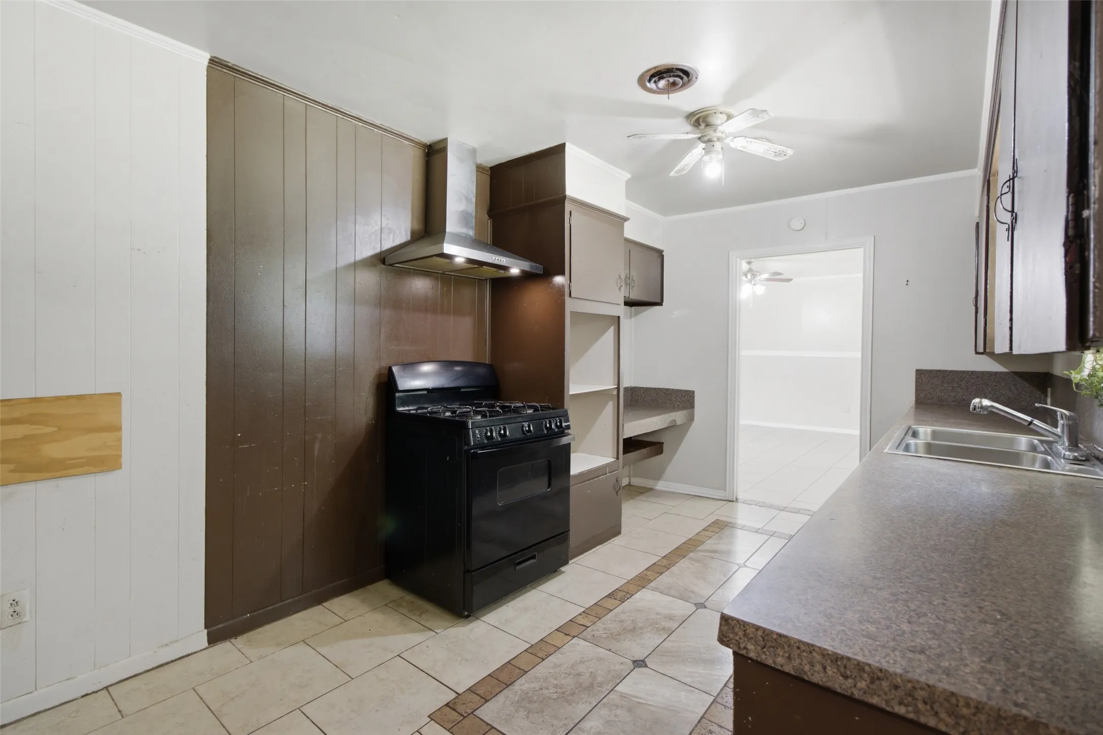Kitchen featuring a stainless steel range hood, black freestanding gas range, tile flooring with decorative accents, an undermount double basin sink, and a ceiling fan with integrated lighting