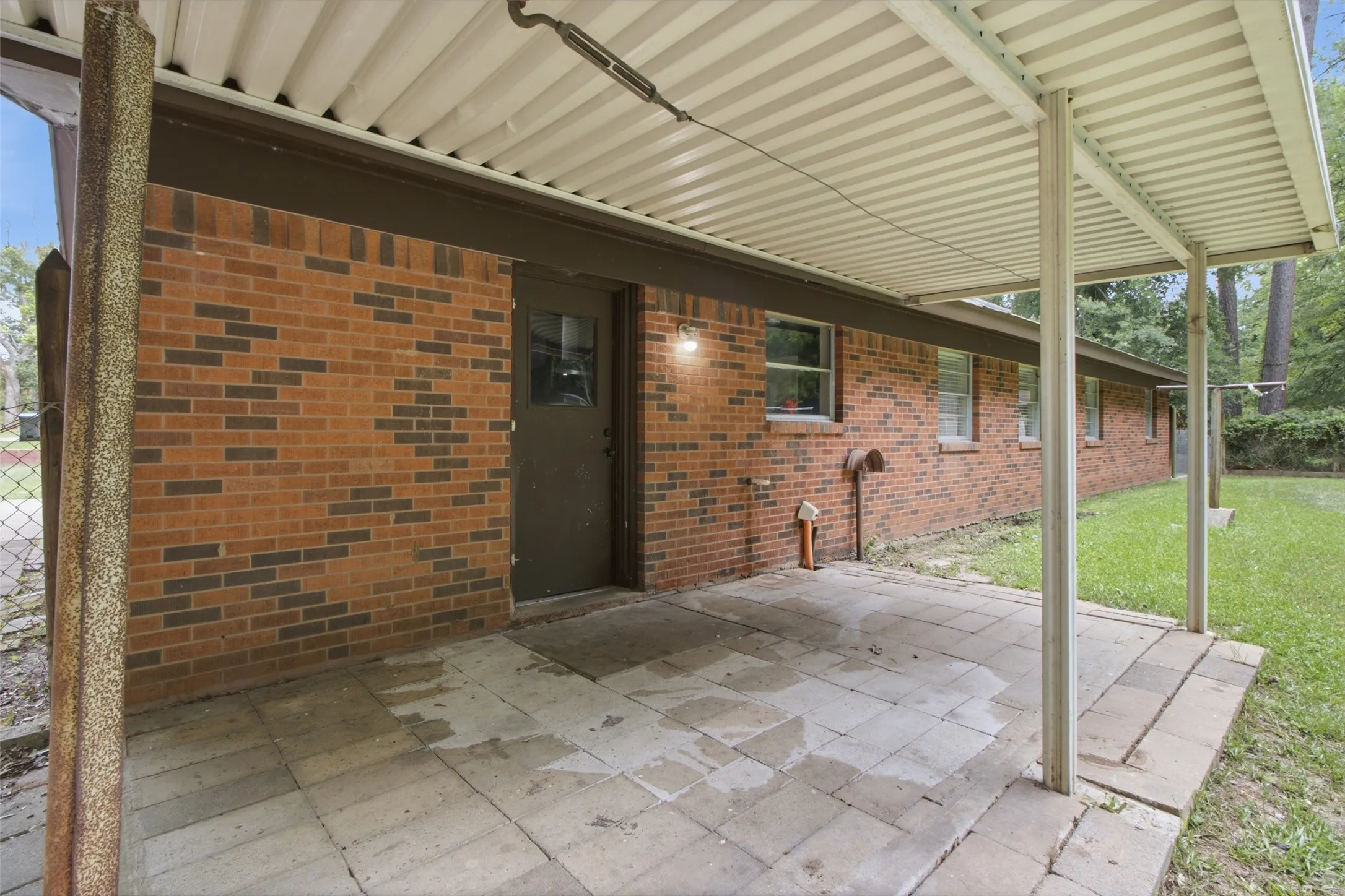 Covered patio featuring a corrugated metal roof, brick exterior, and paver flooring