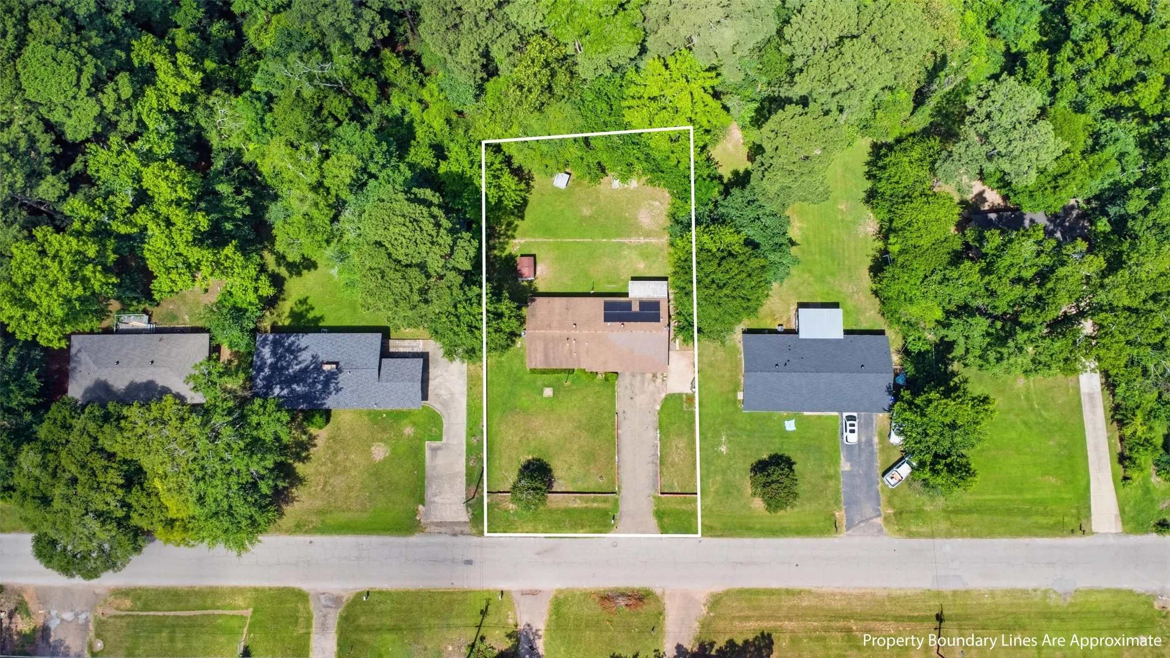 Aerial view of a residential property with a detached home, surrounded by mature trees