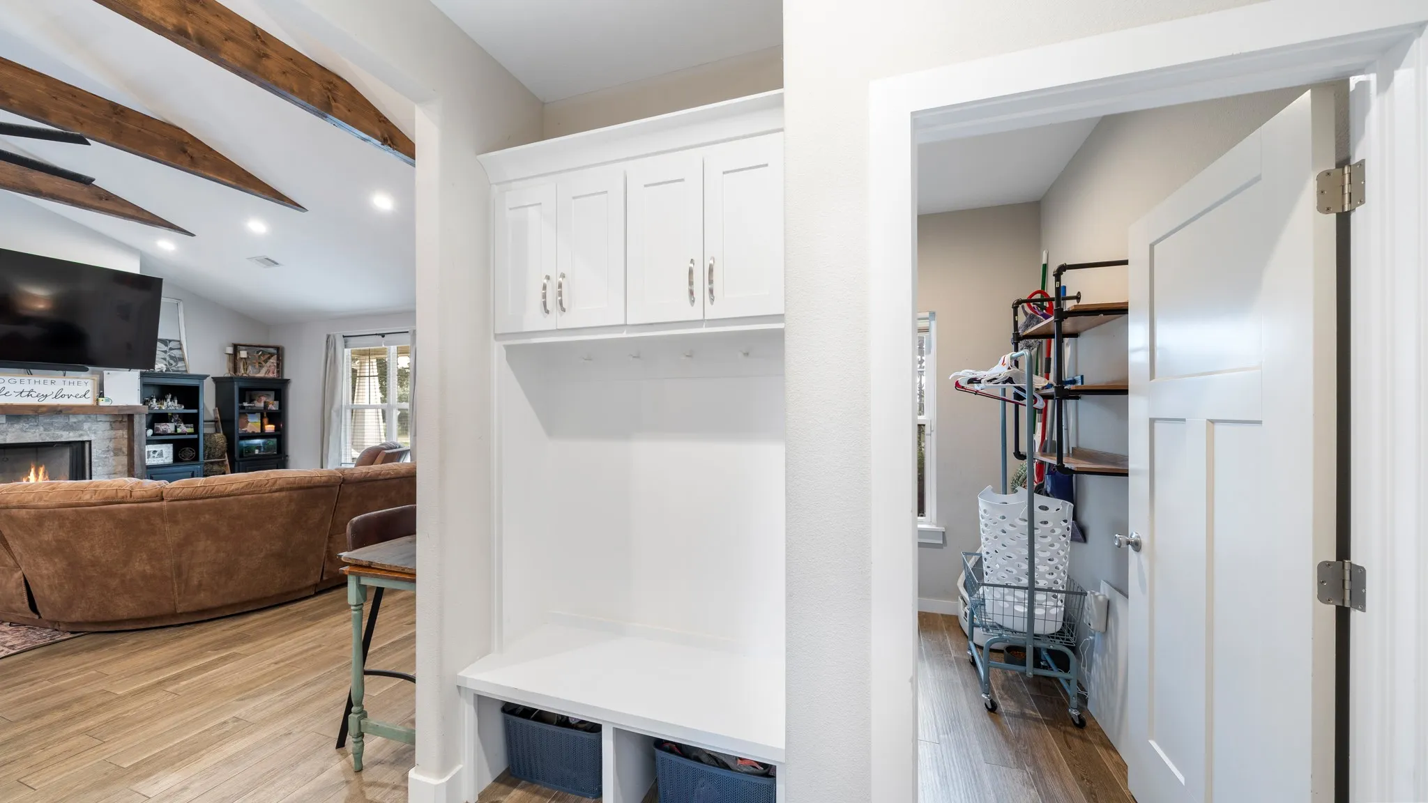 Built-in white cabinetry with gold-toned hardware, wood-finish flooring, and exposed ceiling beams
