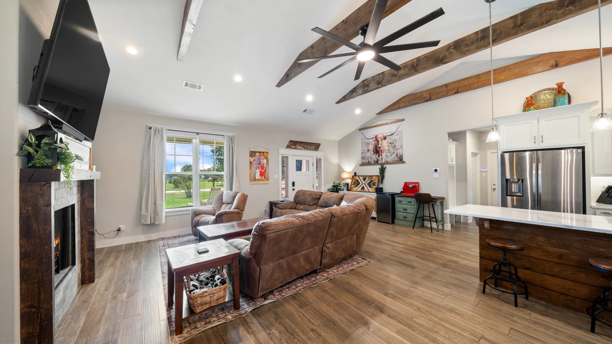 Vaulted ceilings with exposed wood beams, wood-finish flooring, built-in fireplace, recessed lighting, and a kitchen island with white quartz countertop