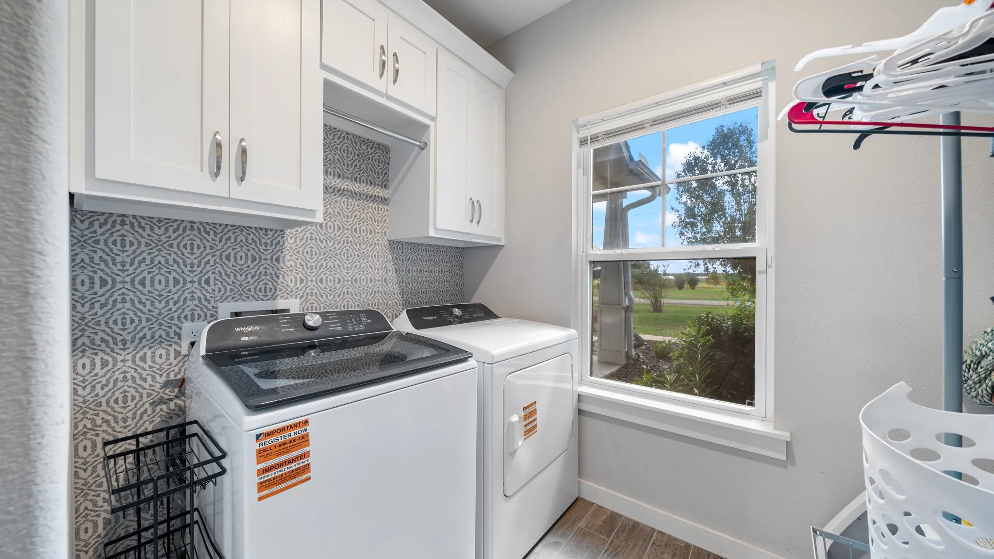 White shaker cabinetry, pattern tile backsplash, wood-finish flooring, and natural light from a double-hung window